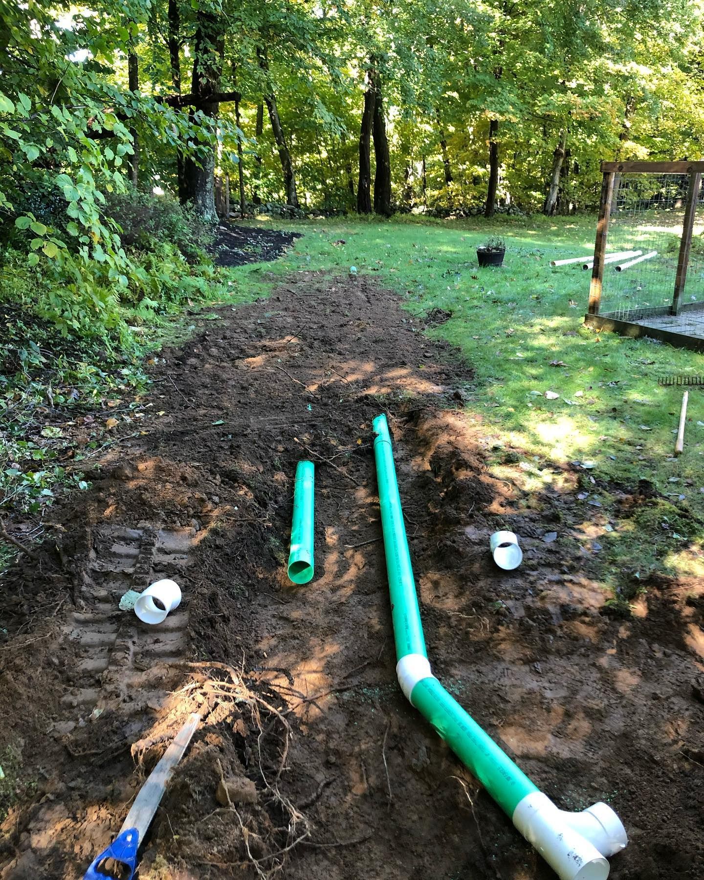 A green pipe is sitting in the dirt next to a saw.