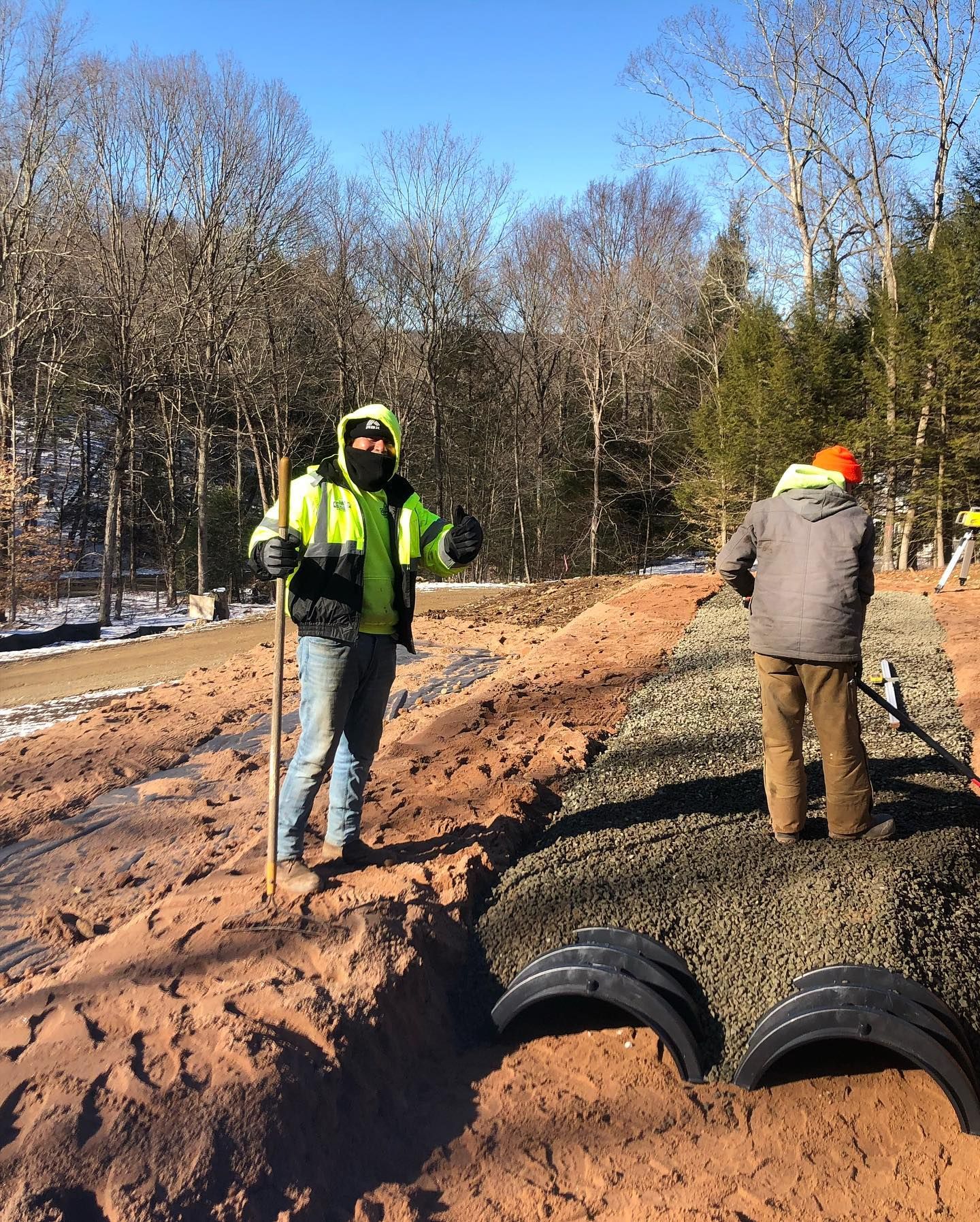 Two men are covering pipes with gravel.