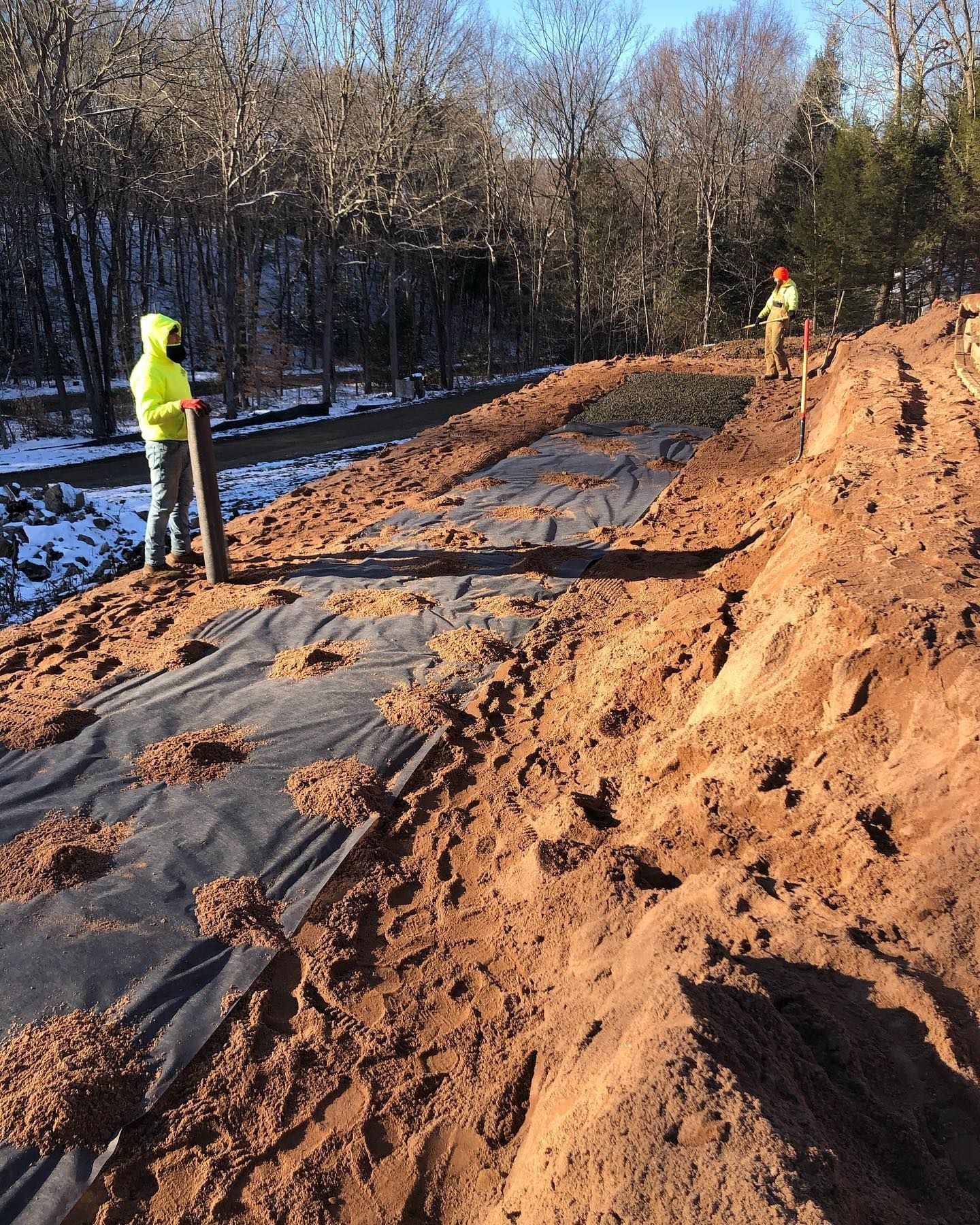 A man in a yellow jacket is standing on top of a pile of dirt.
