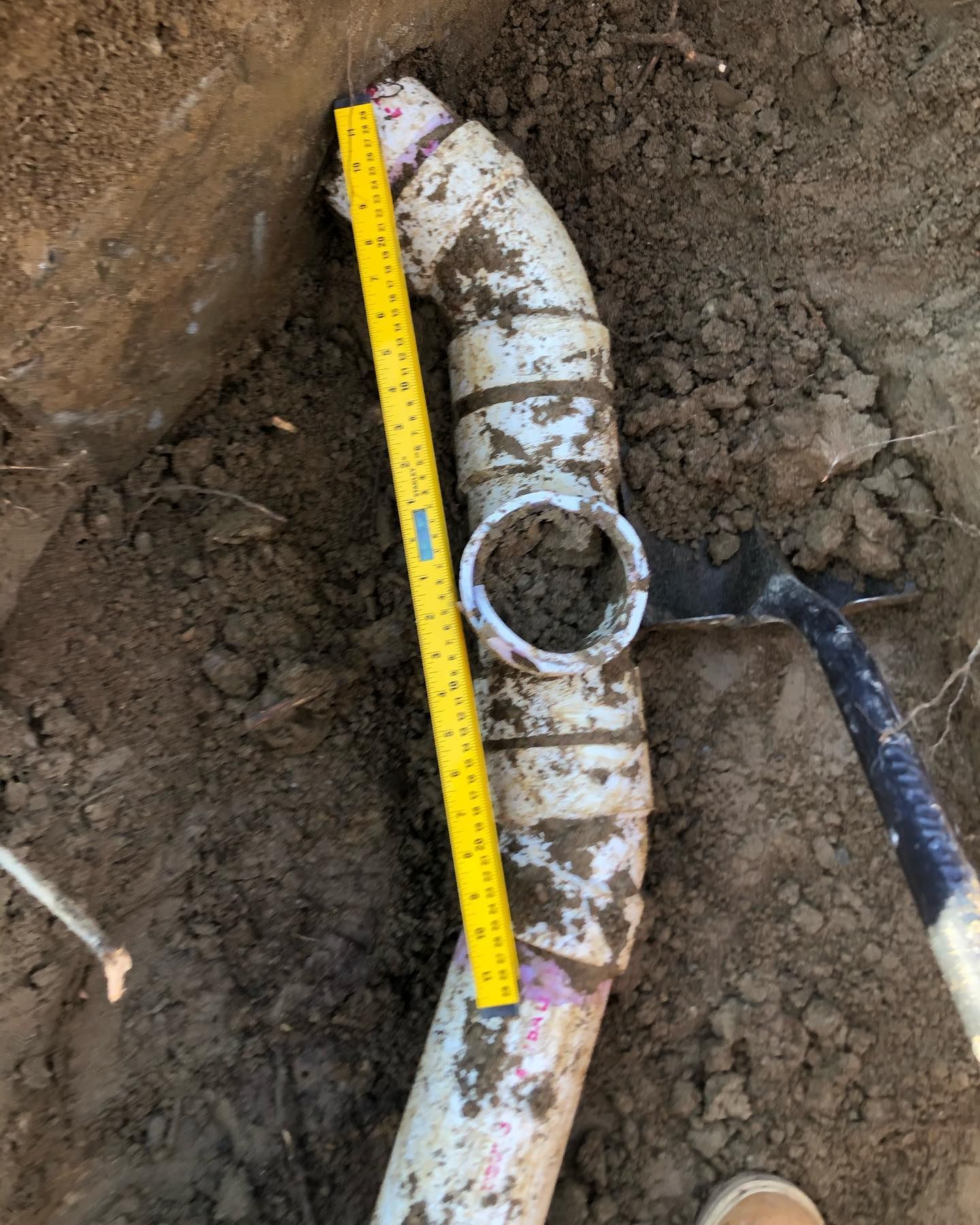 A yellow ruler is measuring a pipe in the dirt.