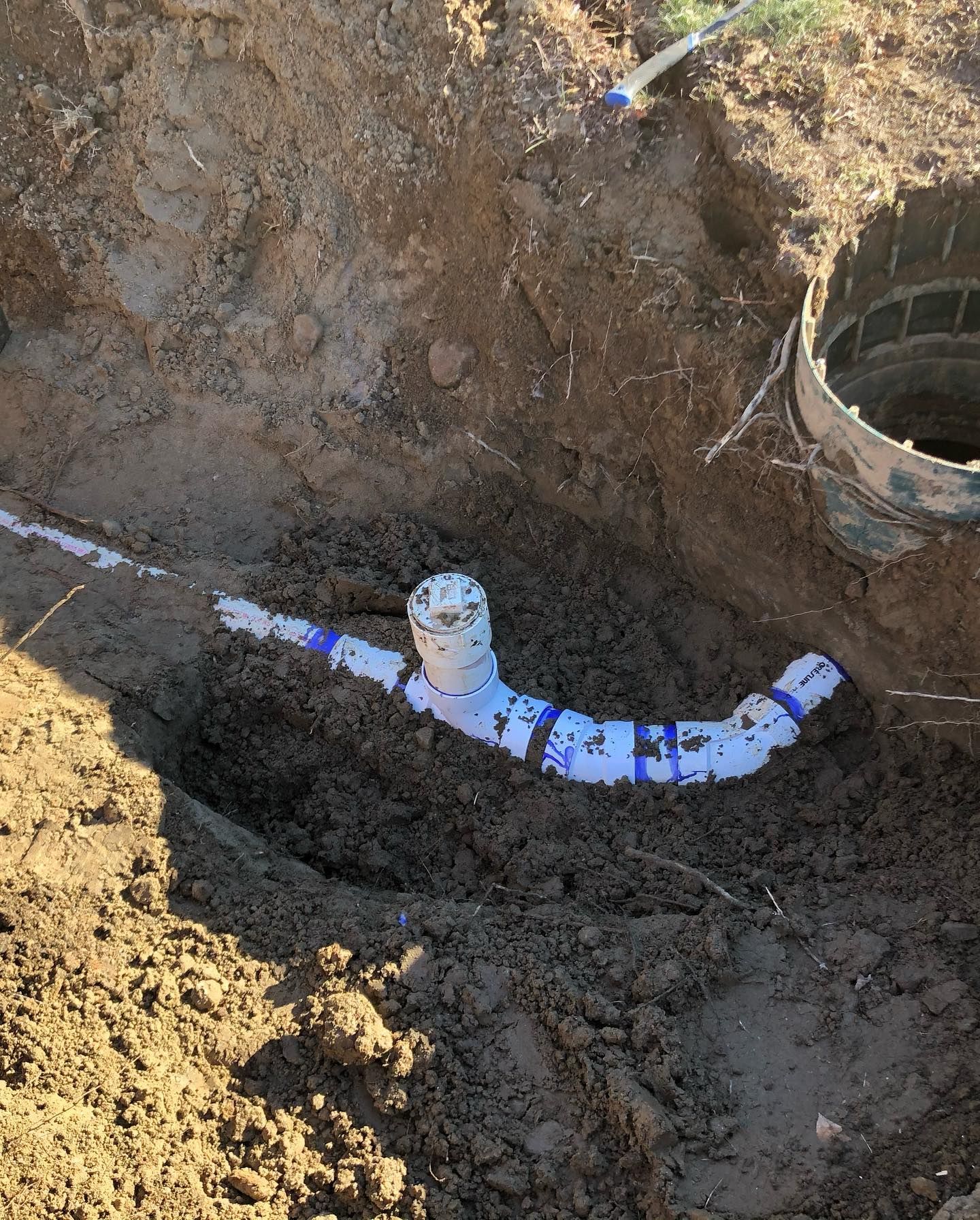 A white pipe is laying in the dirt next to a bucket.