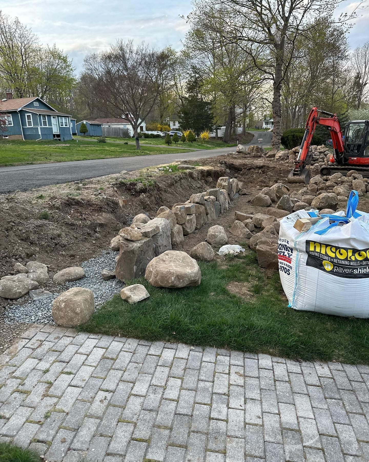 A bag of dirt is sitting on the grass next to a brick walkway.