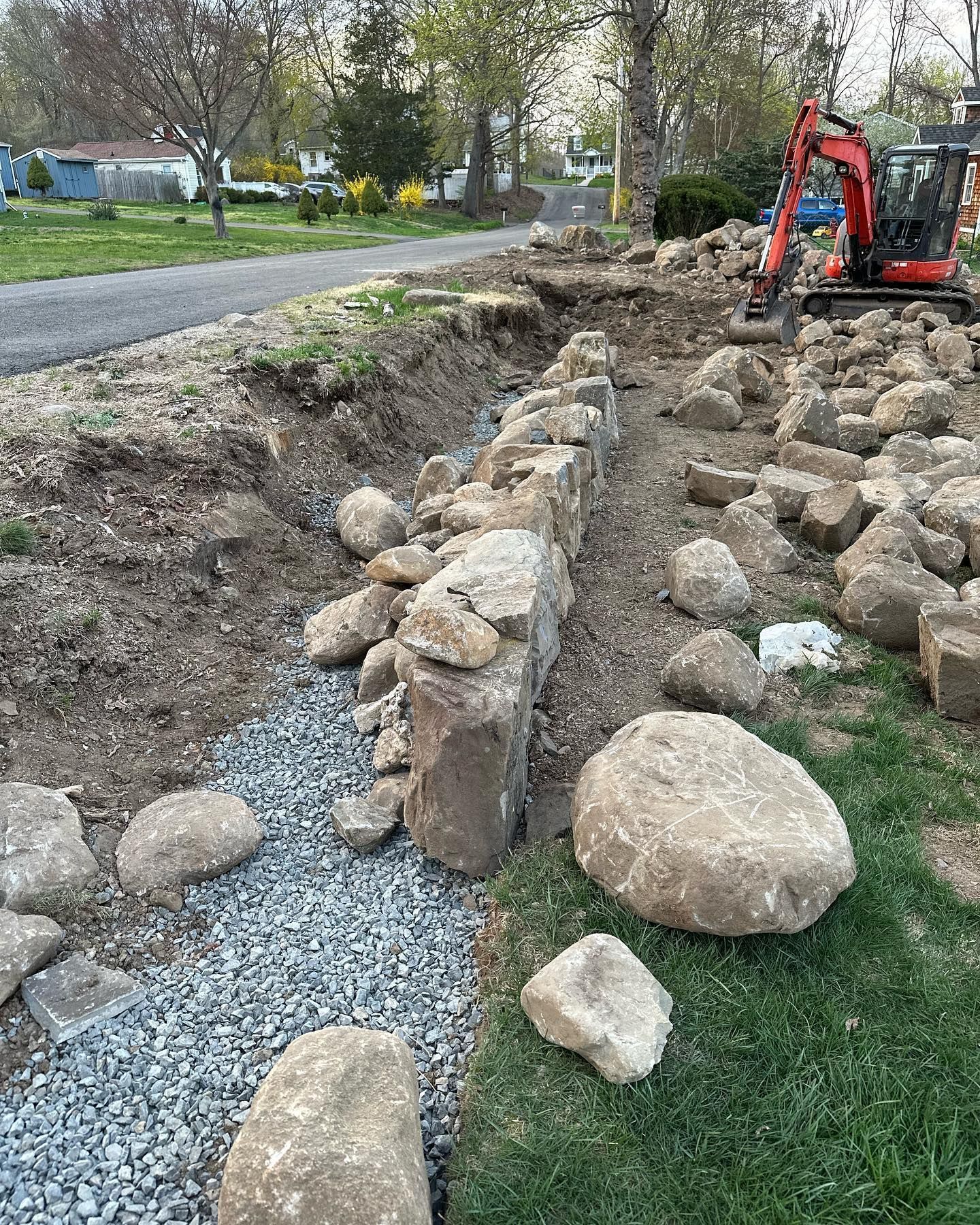 A small excavator is working on a rock wall in a yard.