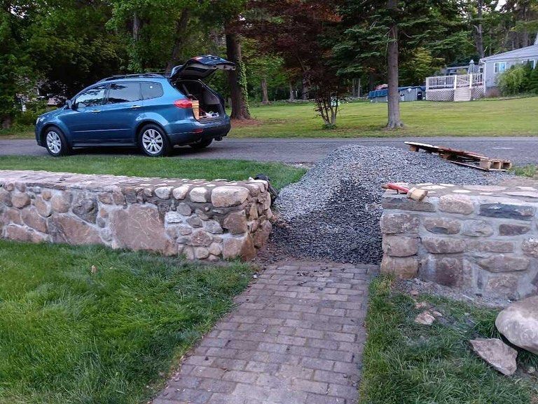 A blue suv is parked on the side of the road next to a stone wall.