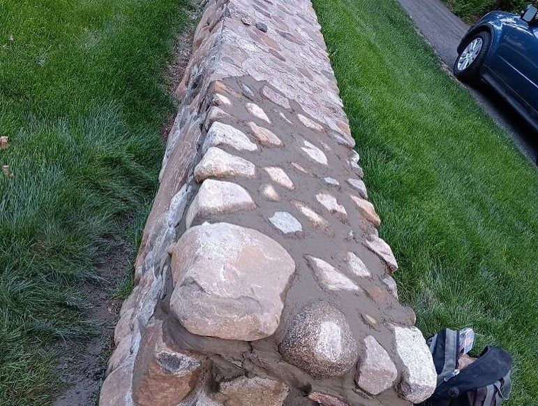 A stone wall is being built in a yard next to a car.