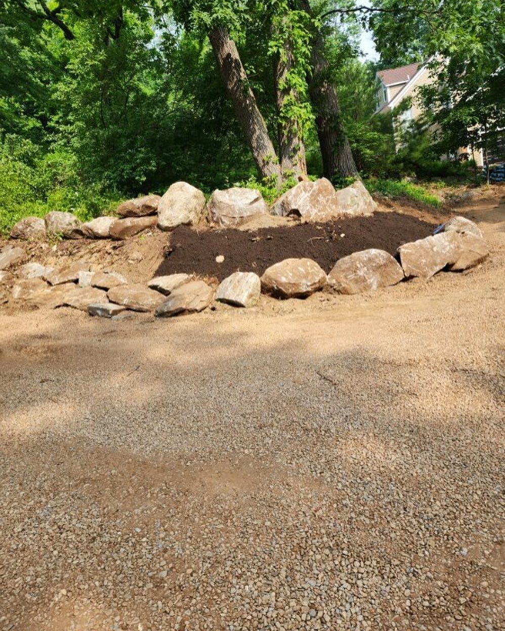 A gravel driveway with rocks in the middle of it and trees in the background.