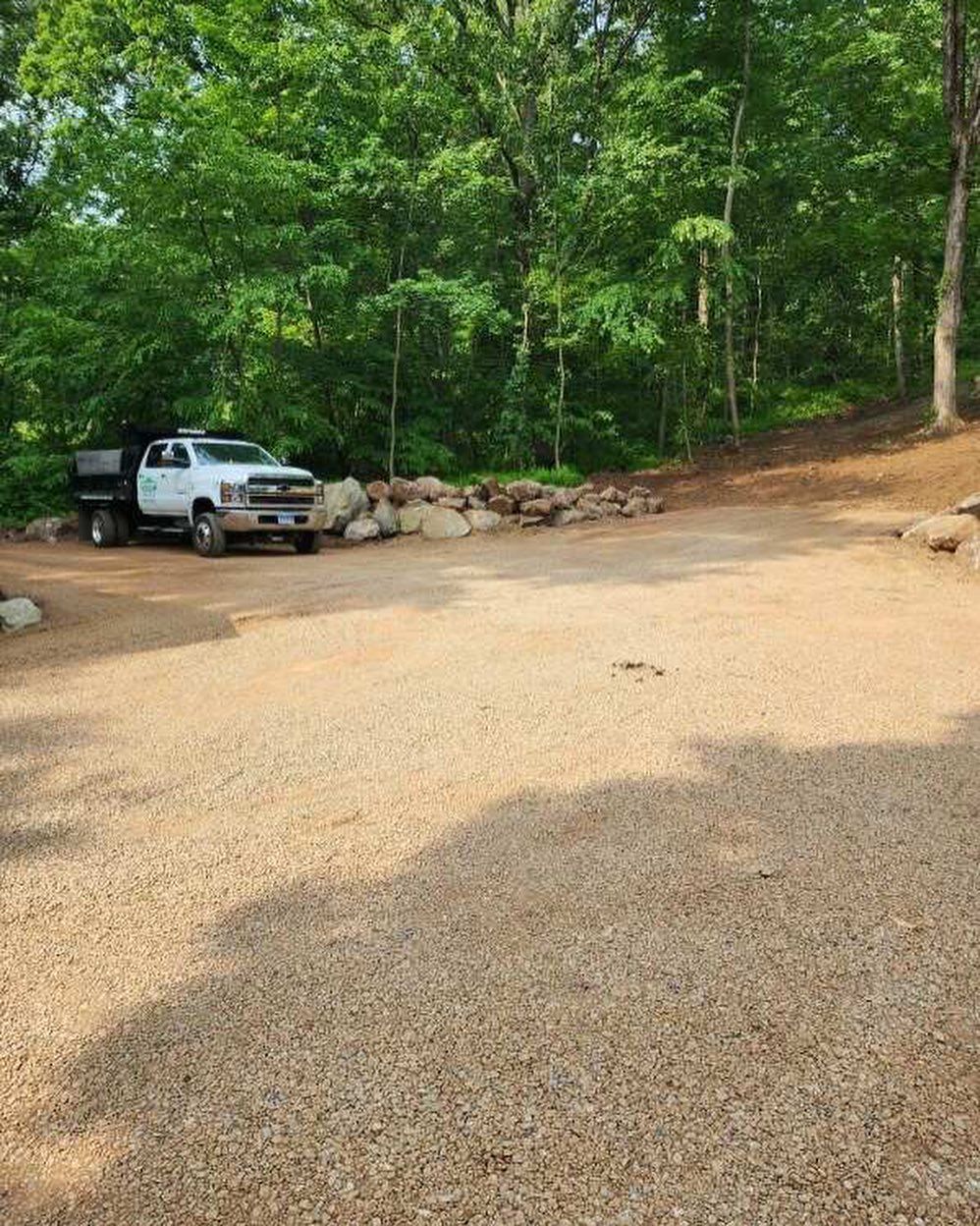 A dump truck is parked in a gravel lot in the woods.