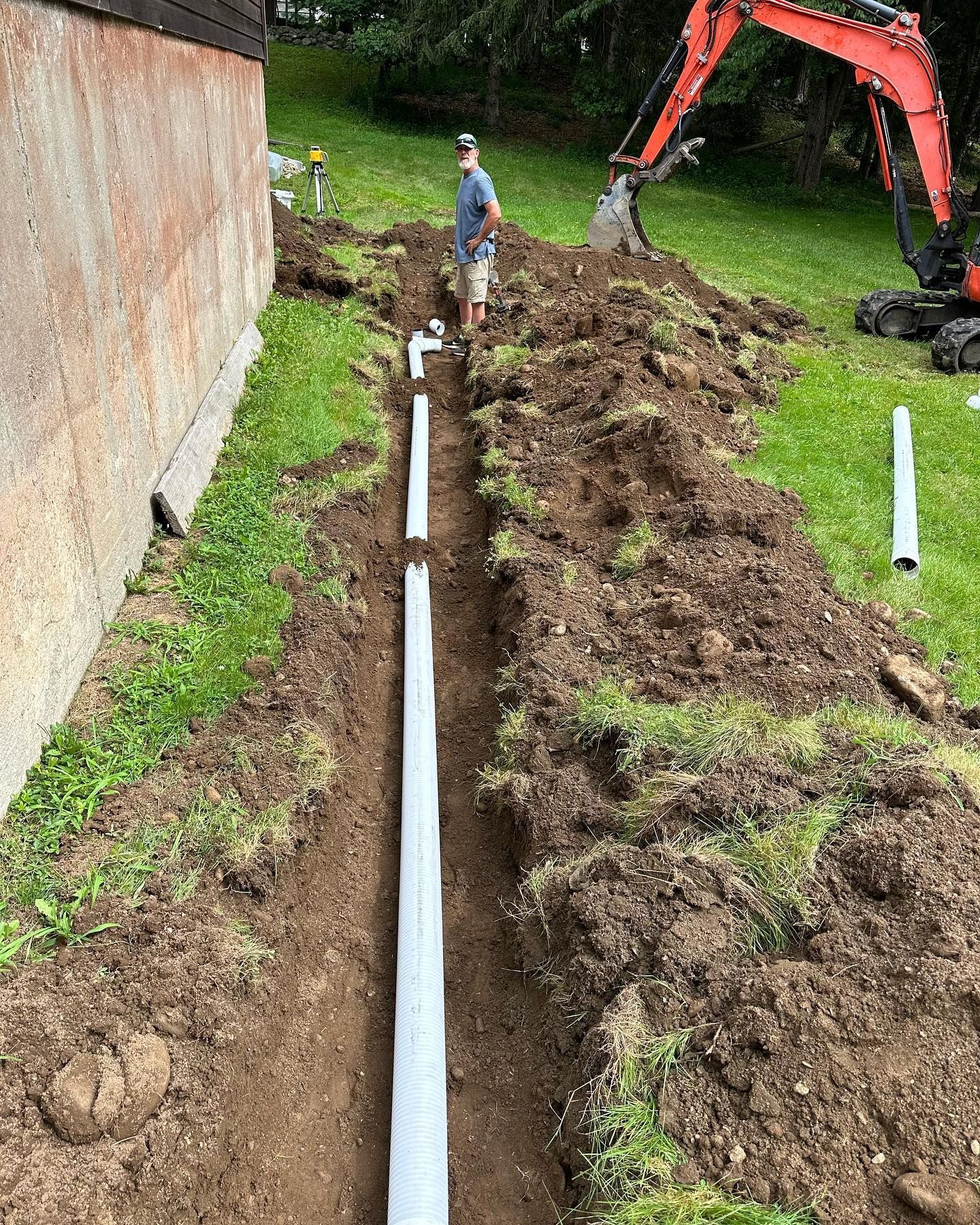 A man is standing in the dirt next to a large pipe.