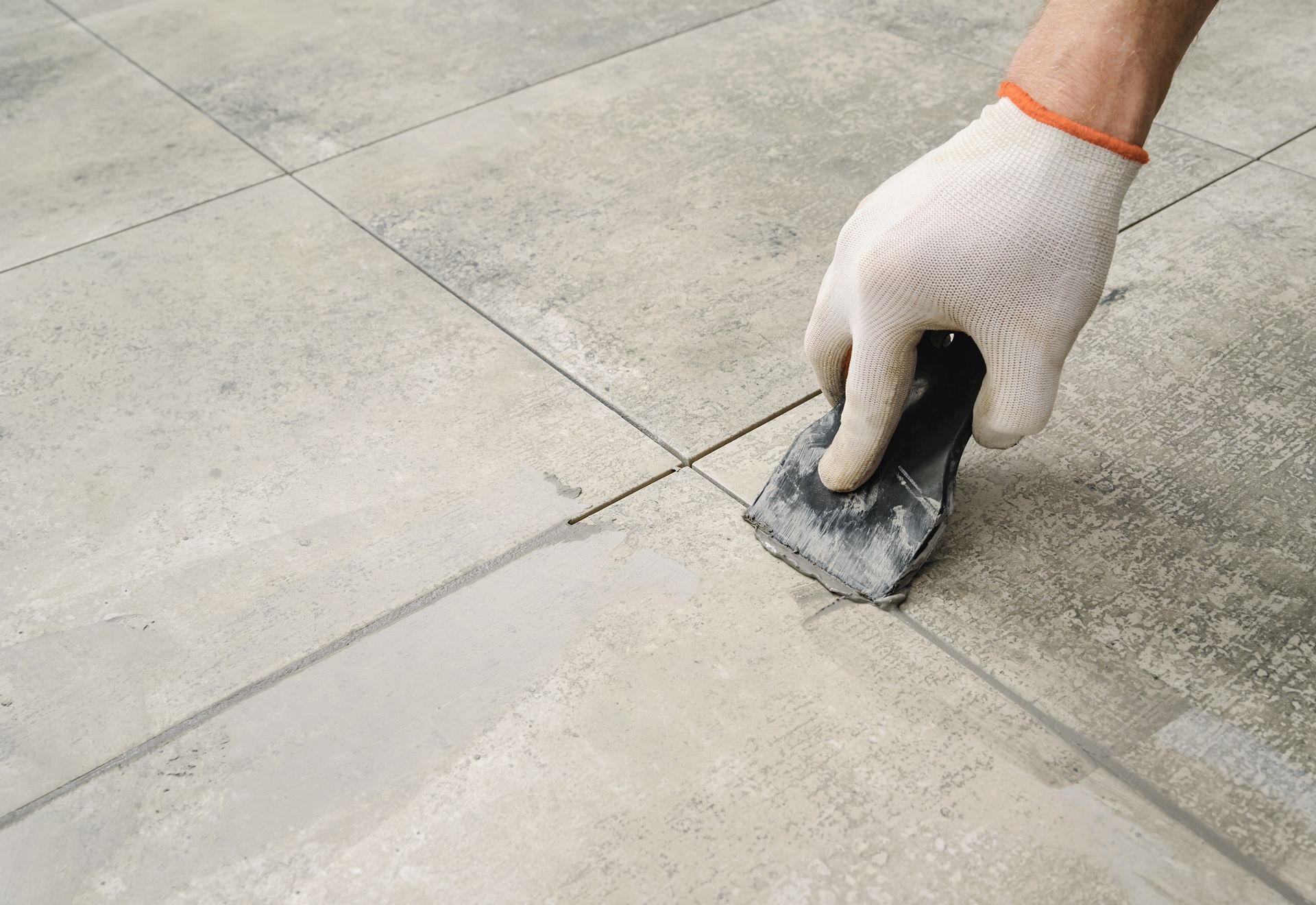 a person wearing a white glove is applying grout on a tile floor