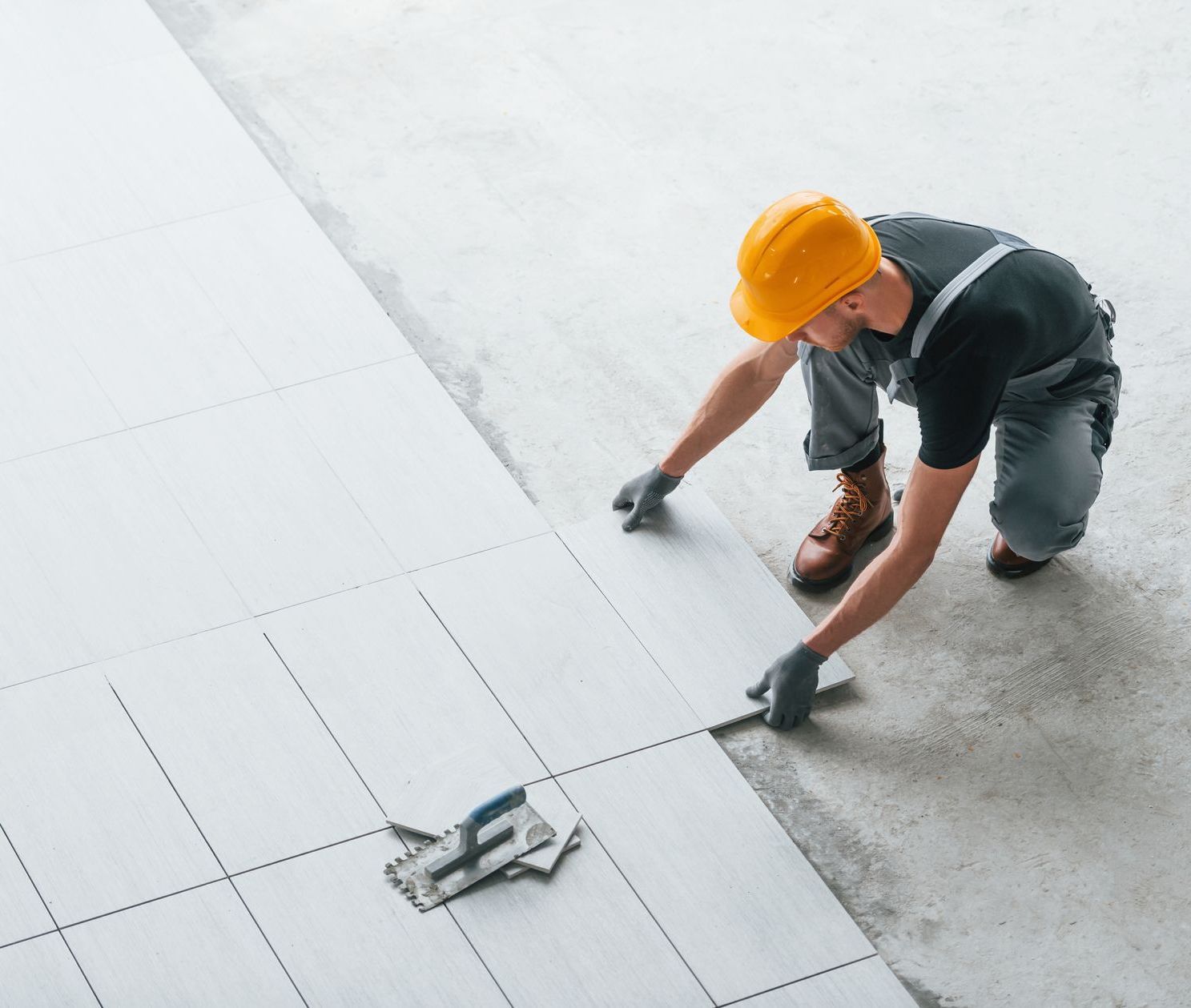 a man wearing a hard hat is laying tiles on the floor