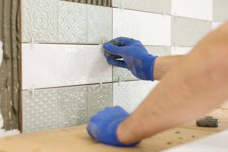 a person wearing blue gloves is installing tiles on a wall