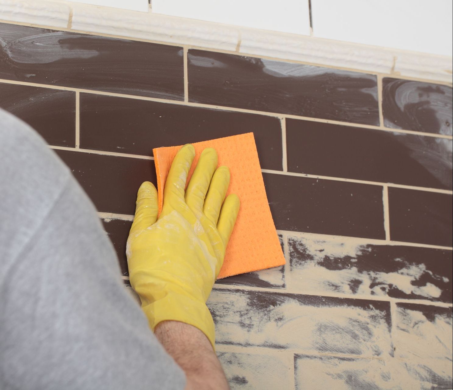 a person wearing yellow gloves is cleaning a tile wall with an orange sponge