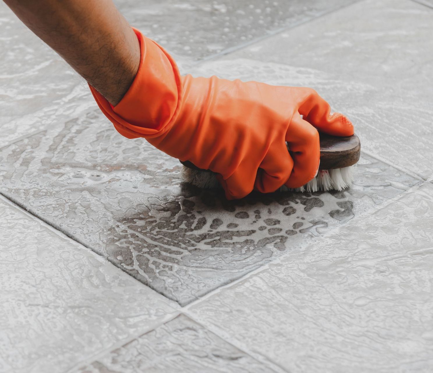 a person wearing orange gloves is cleaning a tile floor with a brush