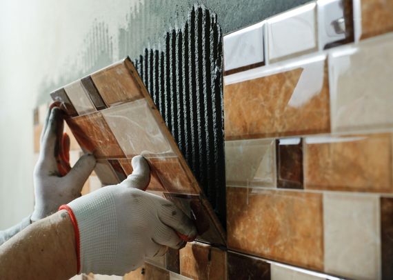 a person wearing gloves is applying tile to a wall