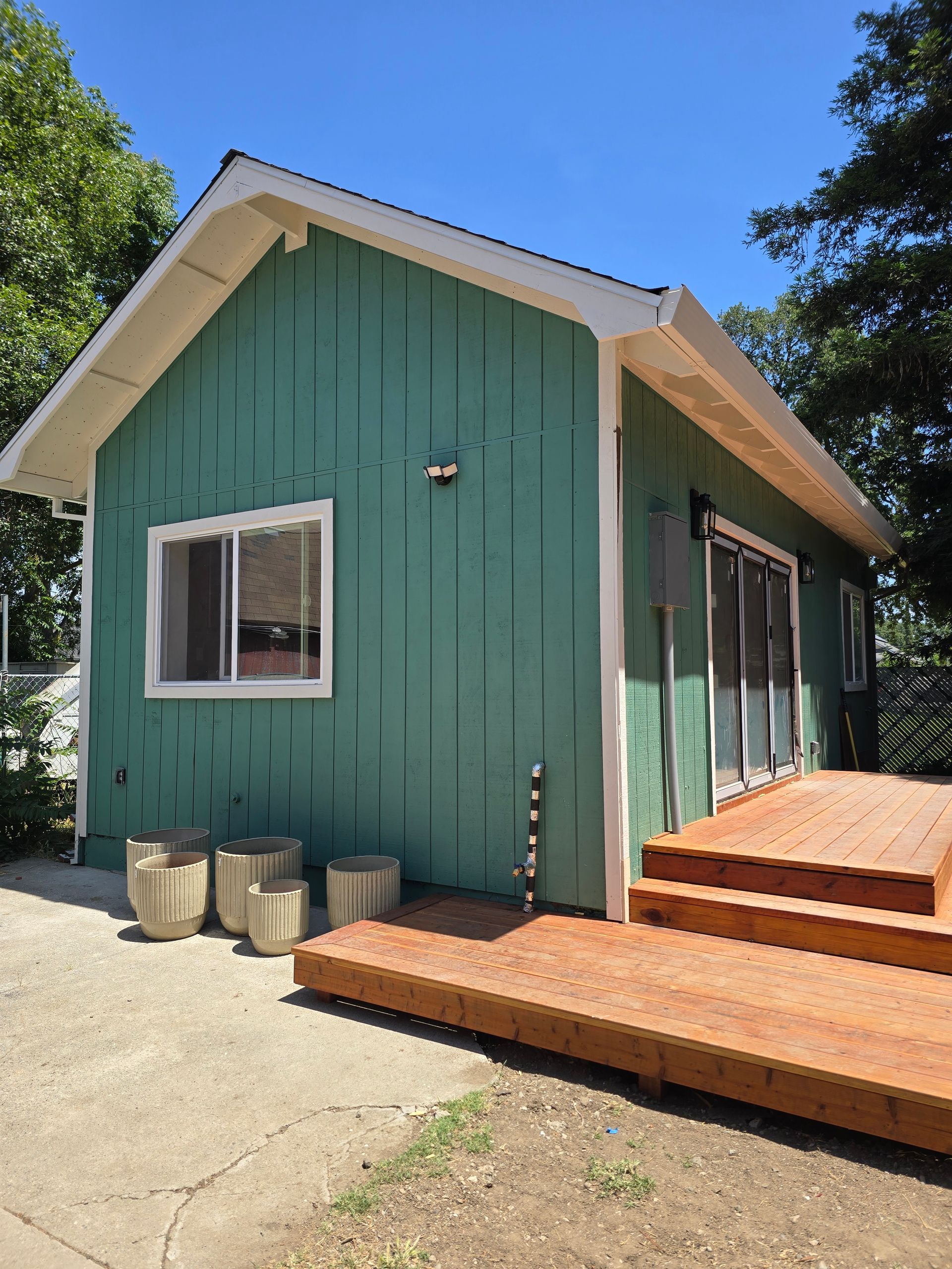 Teal house exterior with white trim, wooden deck steps, and a small window under a blue sky