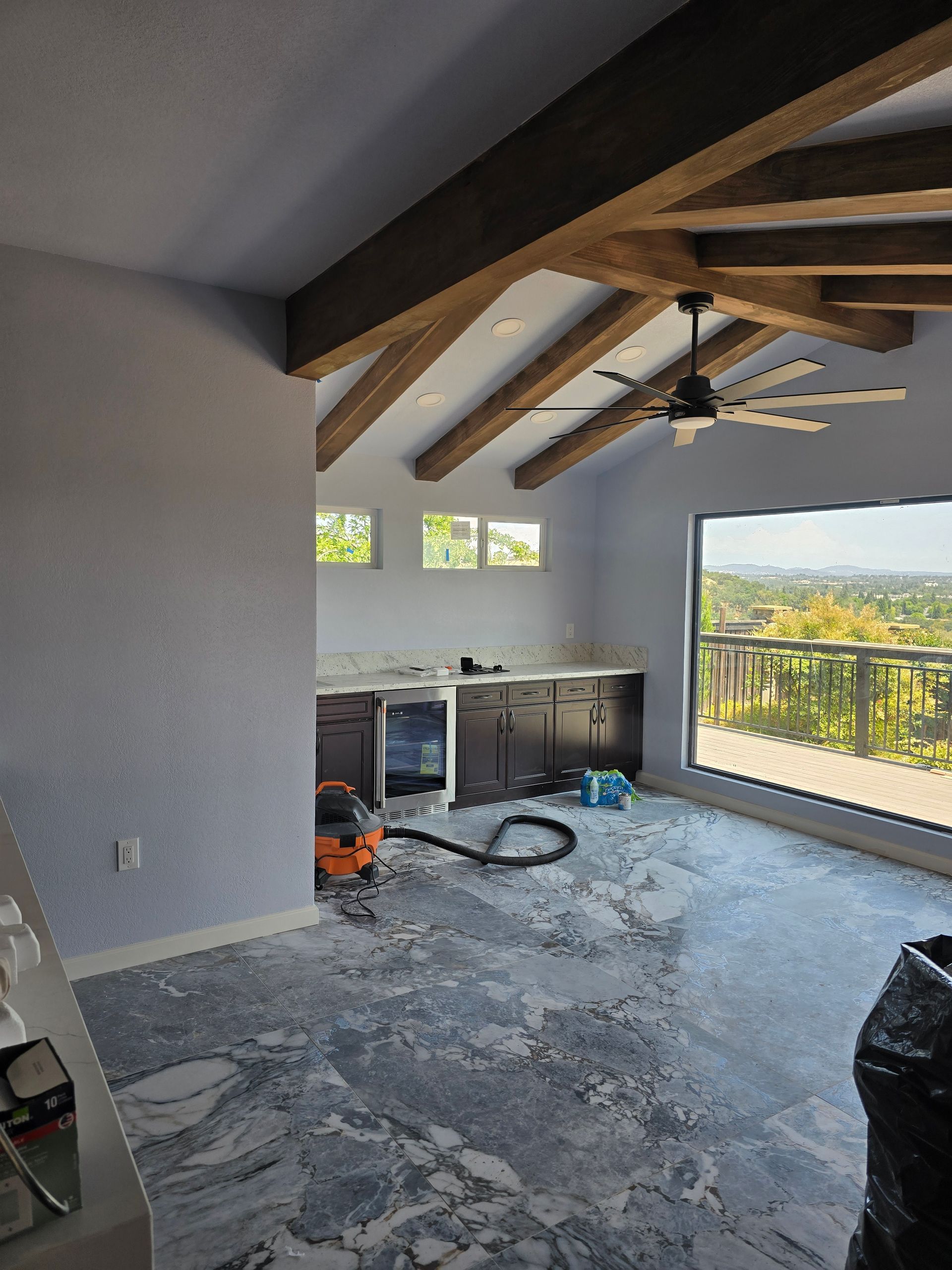 Renovated room with exposed beams, unfinished floor, and large window overlooking a hillside view