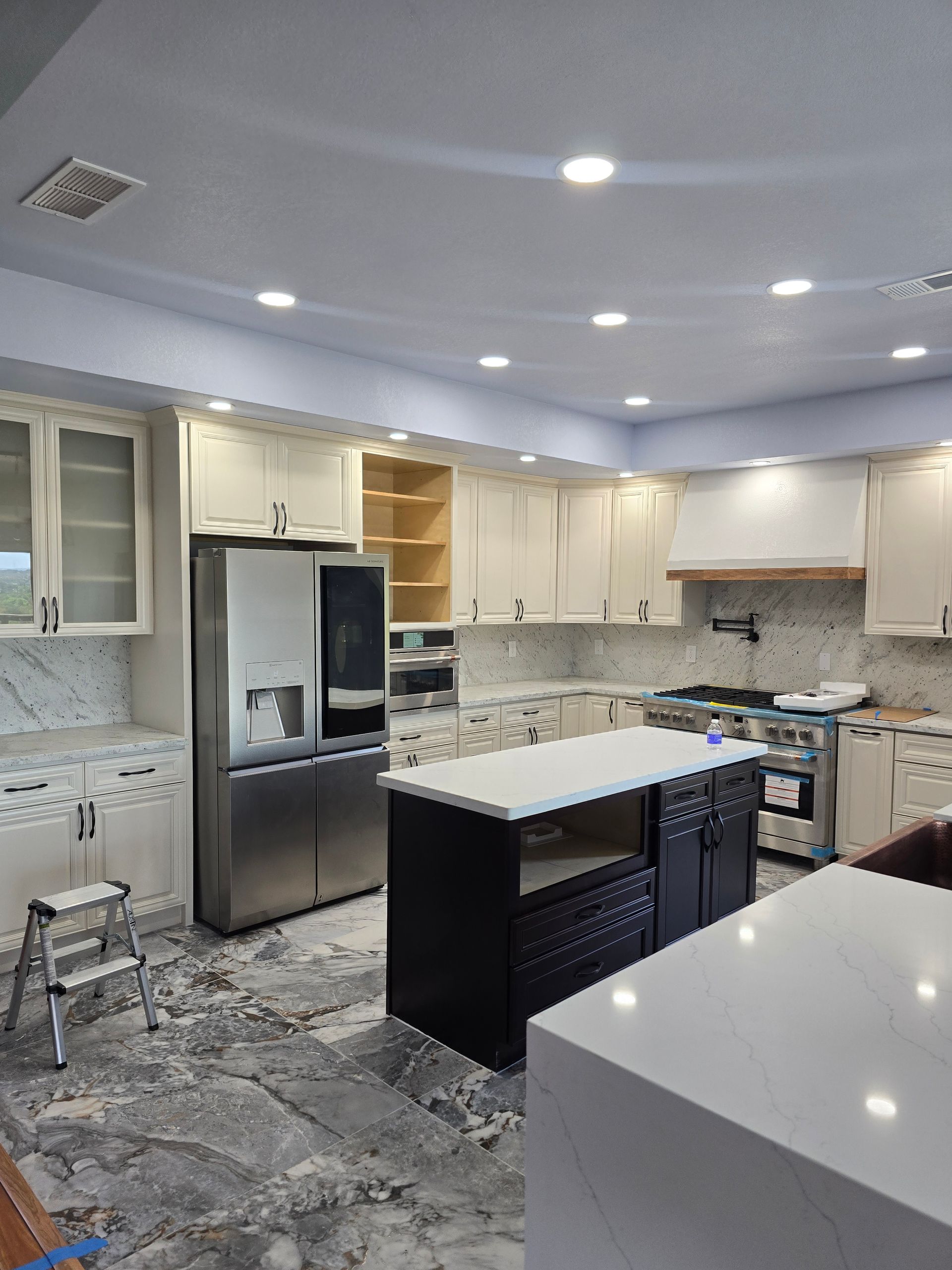 Modern kitchen with stainless steel fridge, white cabinets, island, and gray patterned floor tiles