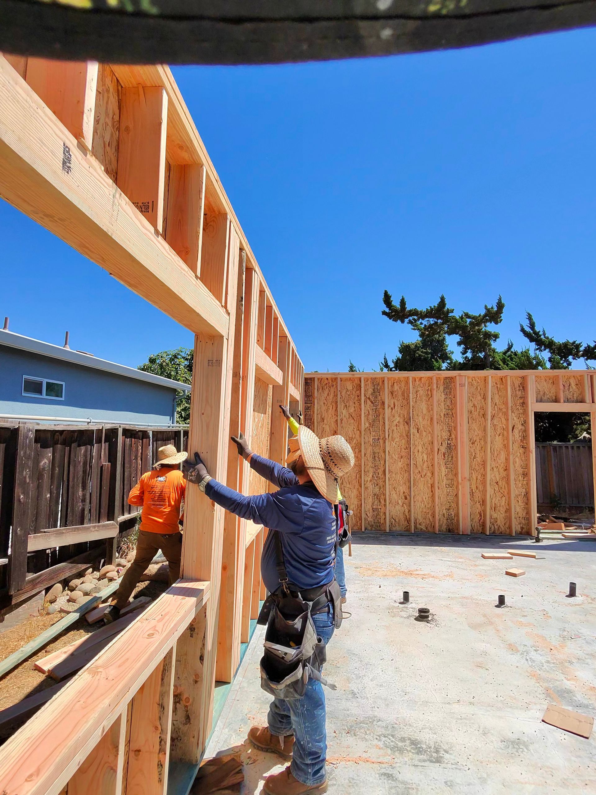 Construction workers framing wooden house walls at a sunny building site