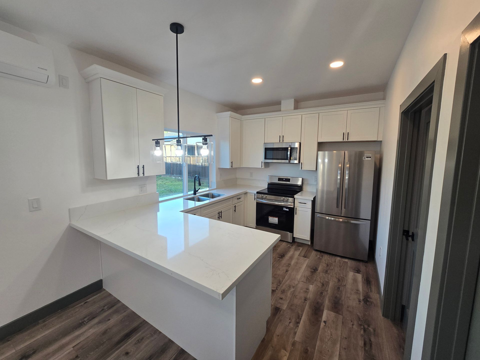 Bright modern kitchen with white cabinets, stainless appliances, island, and dark wood flooring