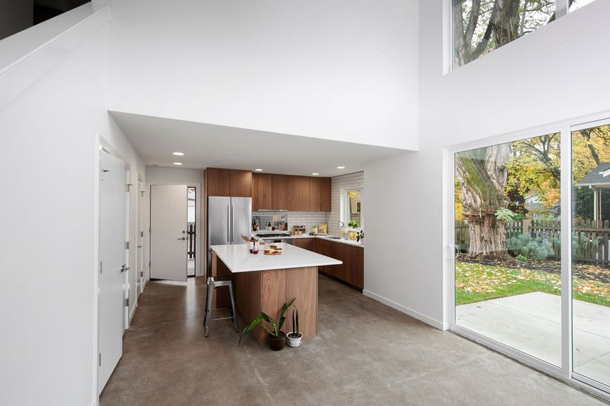Modern open-plan kitchen and living area with wood island, white walls, and sliding glass doors to a garden.