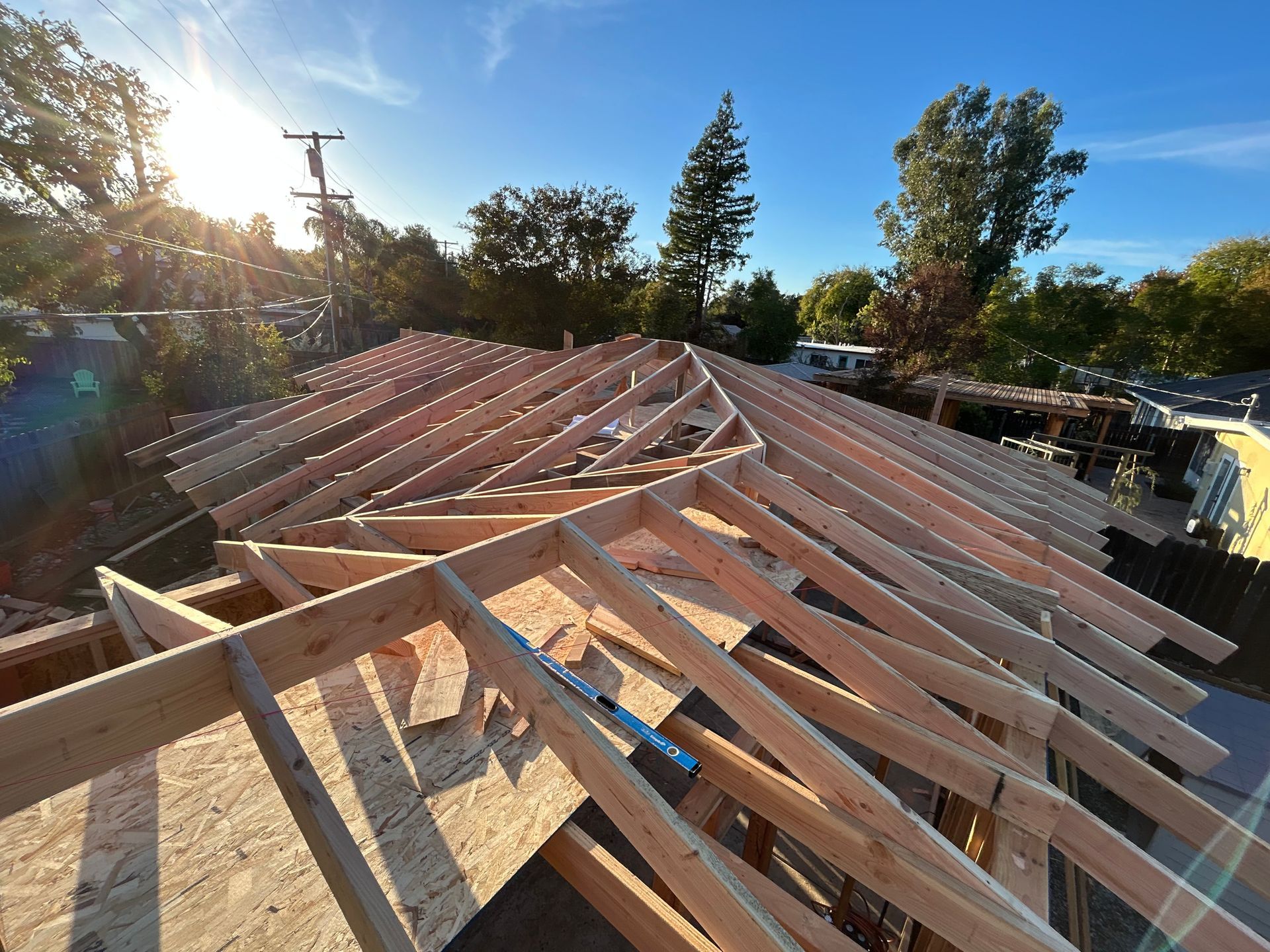 Wooden roof trusses under construction on a house at sunset, with trees and blue sky in the background