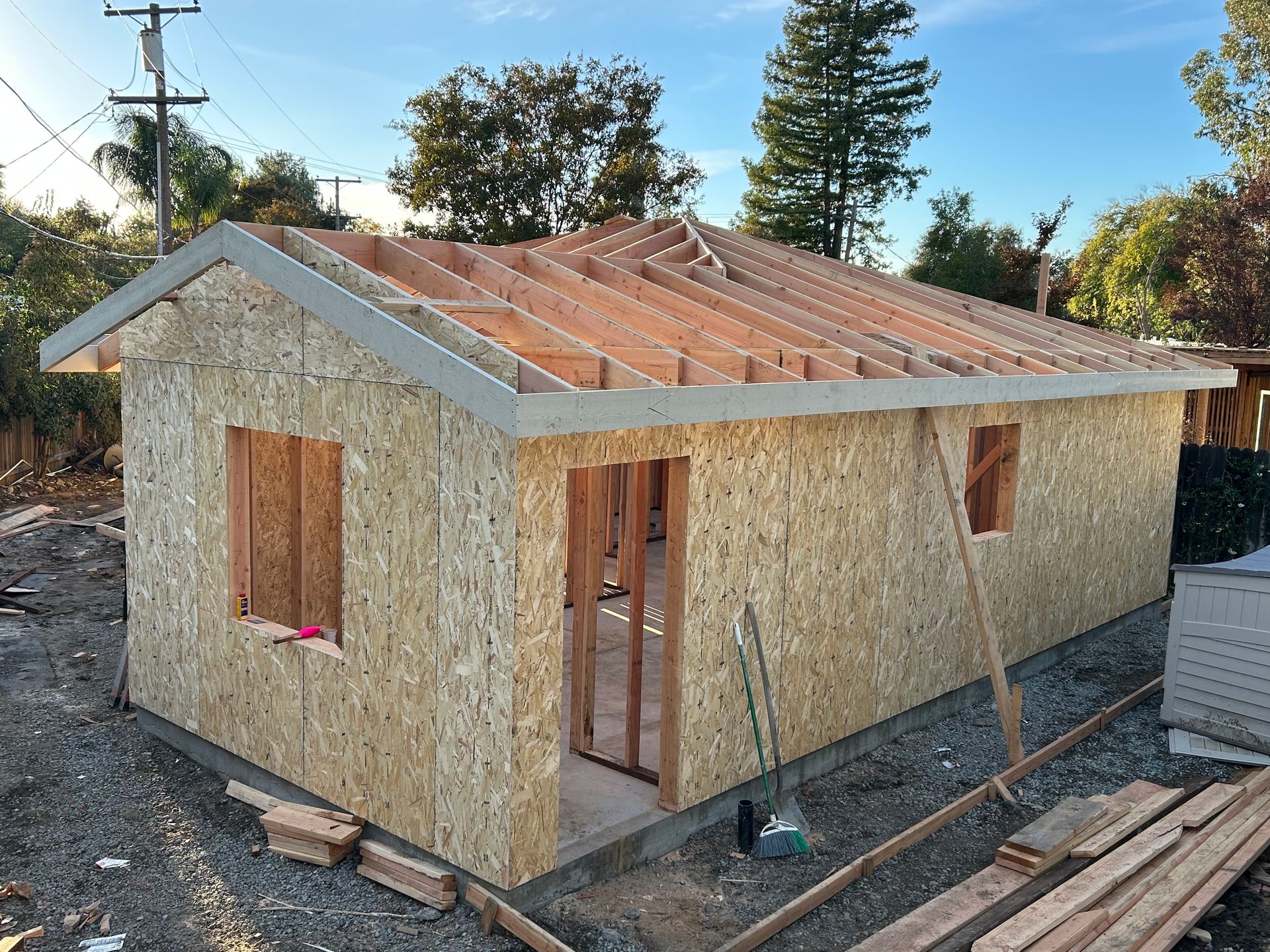 Small unfinished wooden house under construction with boarded windows and a metal roof frame.