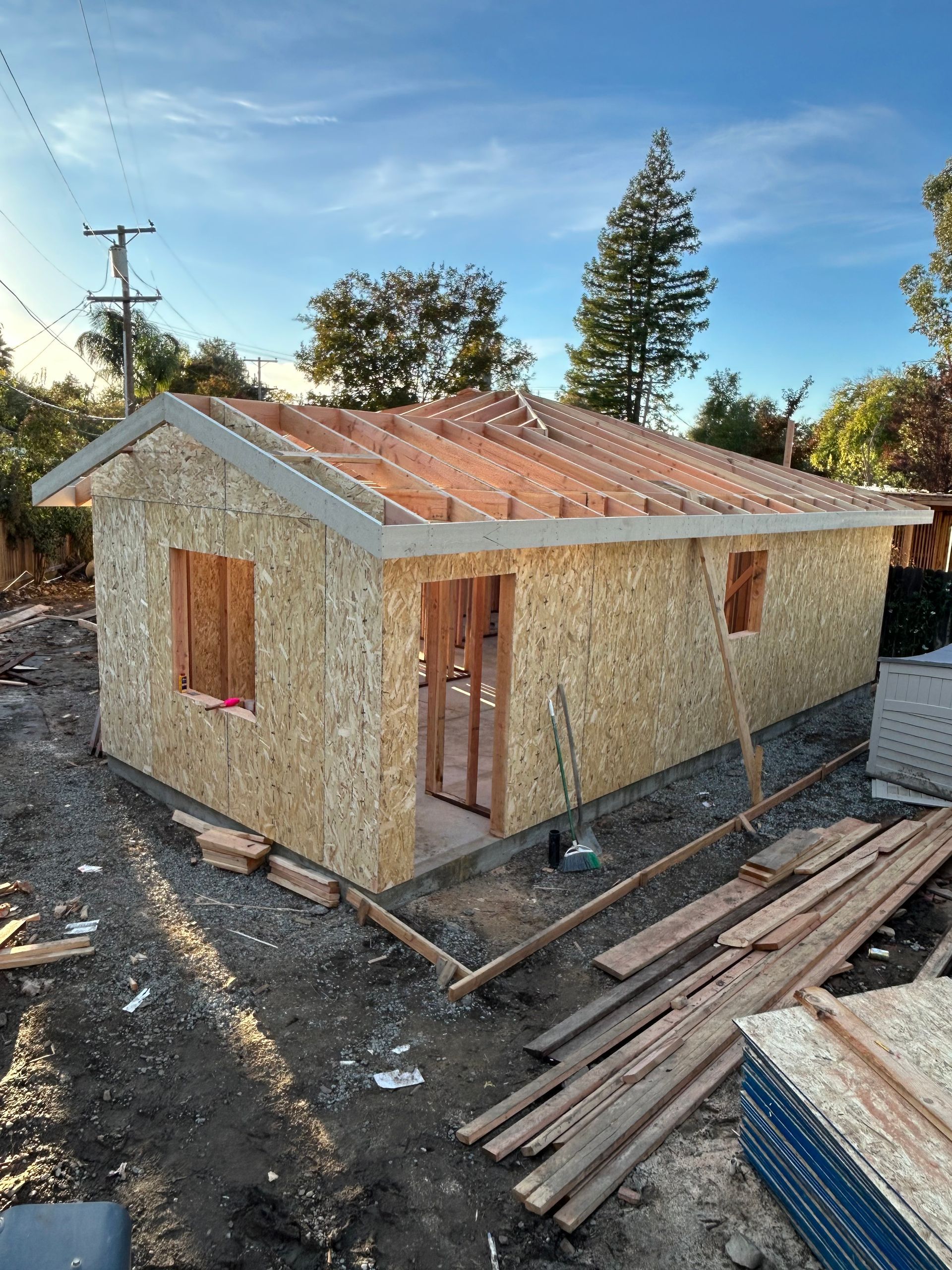 Small unfinished wooden house with a rusted metal roof and boarded windows at a construction site.