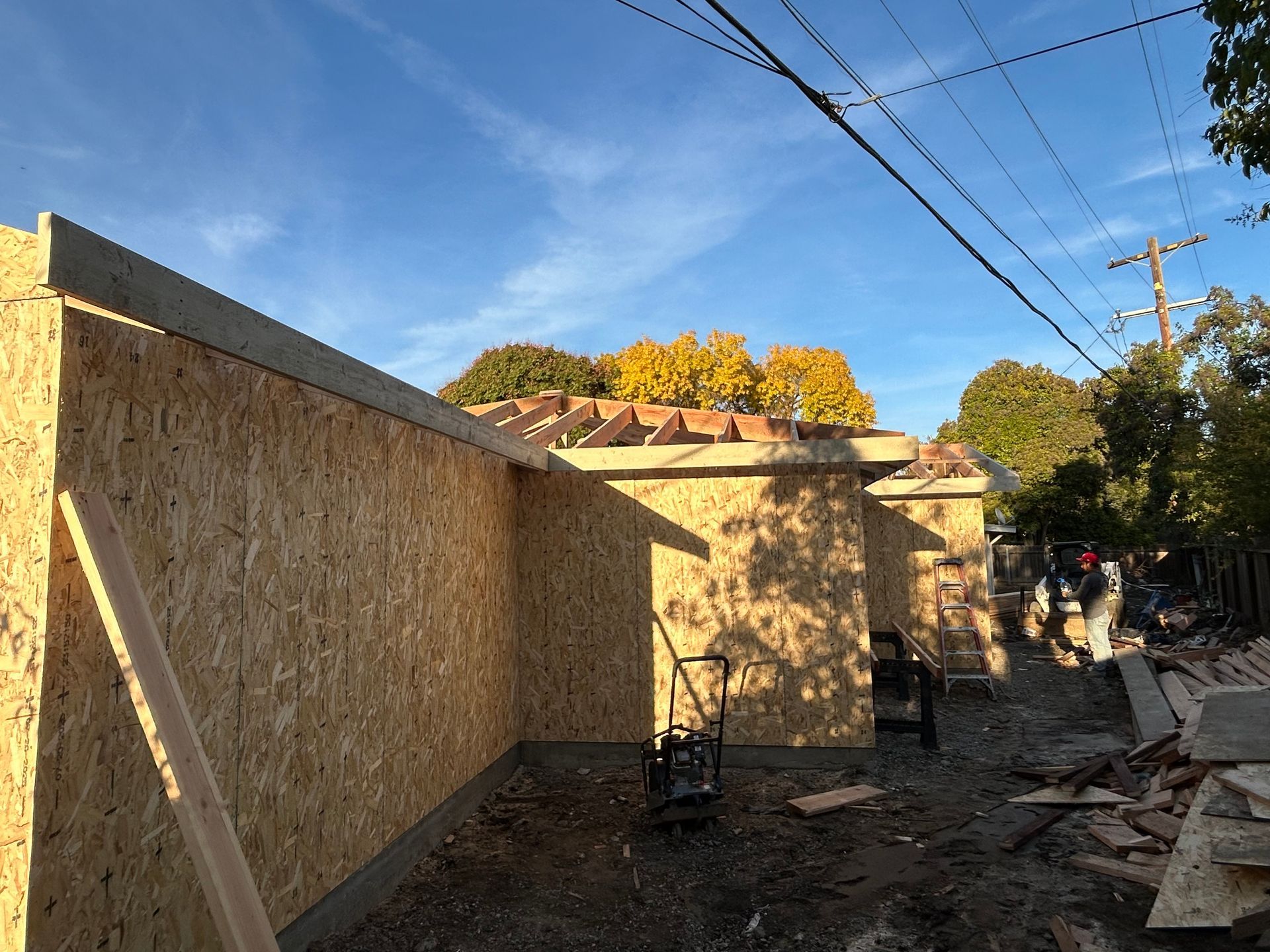 Partially built wooden fence along a dirt alley with tools and debris under a blue sky