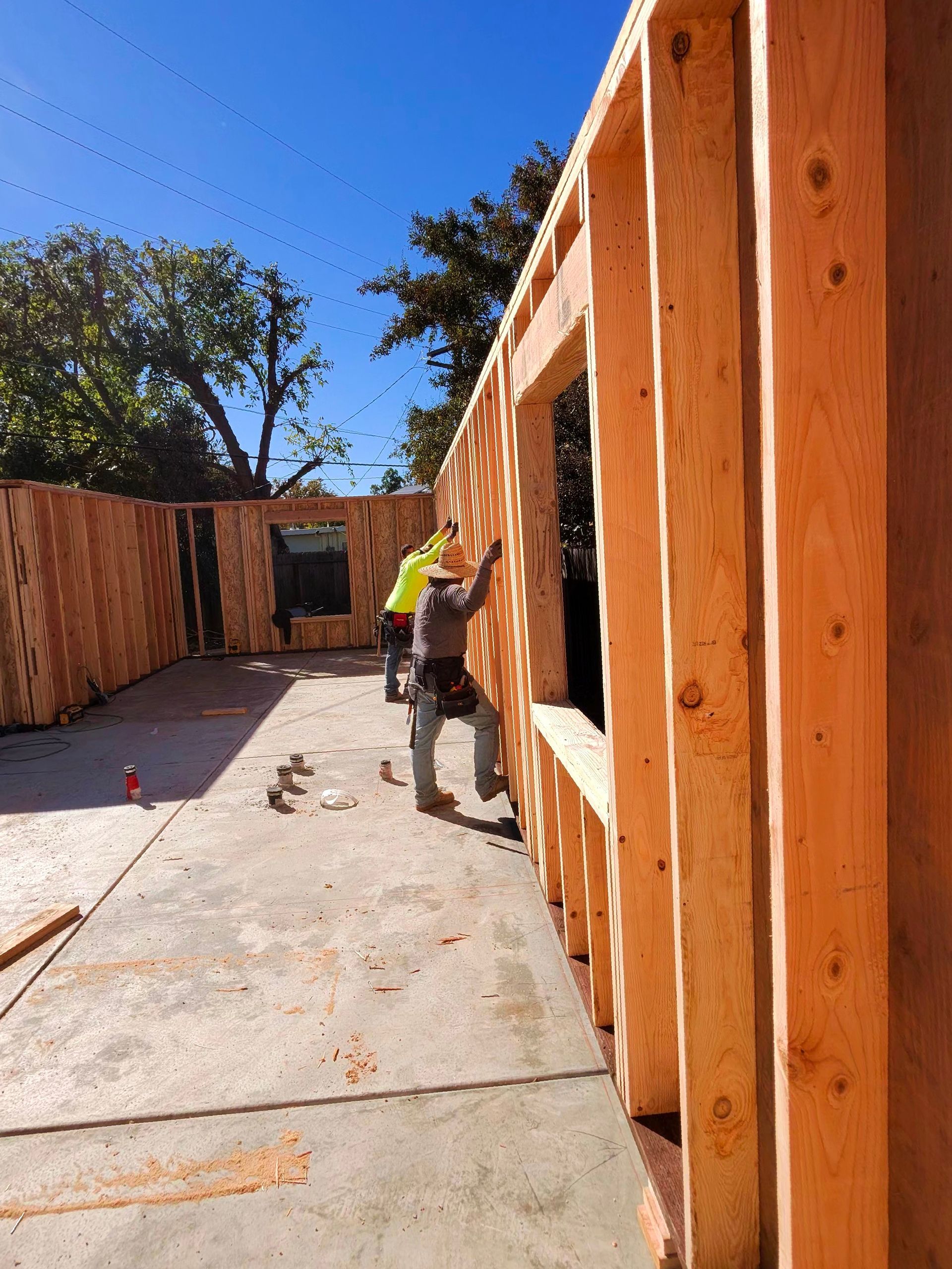 Construction site with wooden framing and a worker measuring a wall in bright sunlight