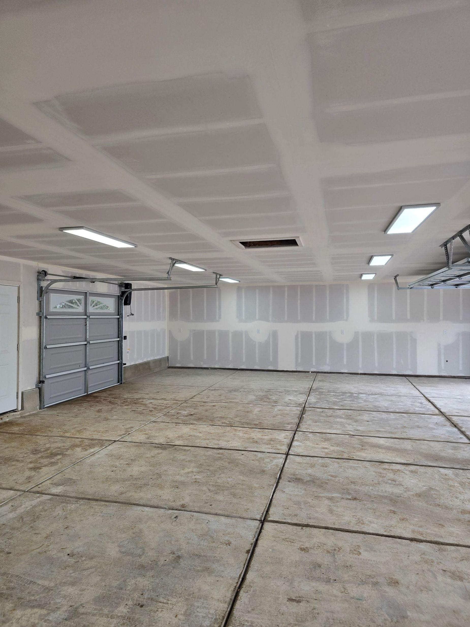 Empty garage interior with unfinished floor, white walls, ceiling lights, and a closed garage door