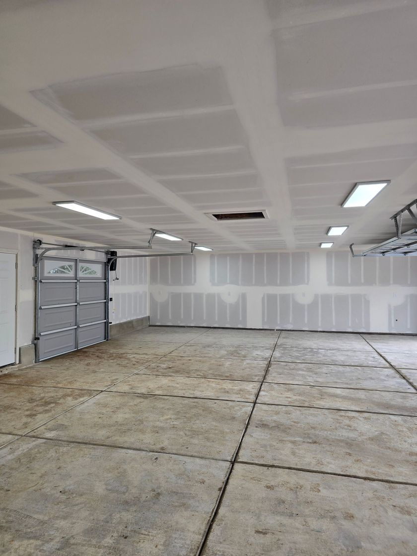 Empty garage interior with unfinished walls, concrete floor, and overhead fluorescent lights
