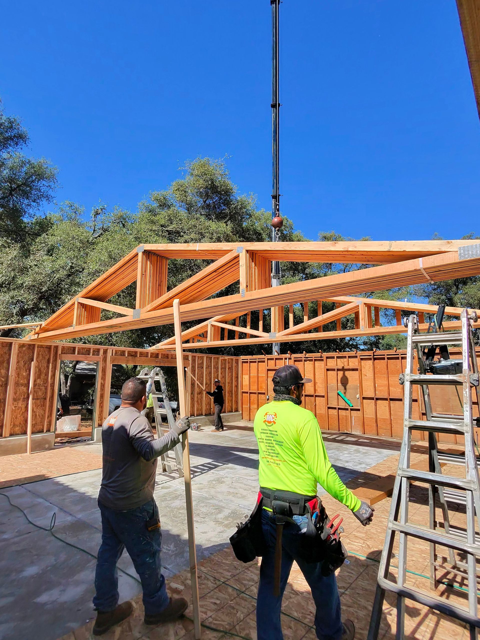 Workers assembling a wooden house frame on a construction site under a blue sky.