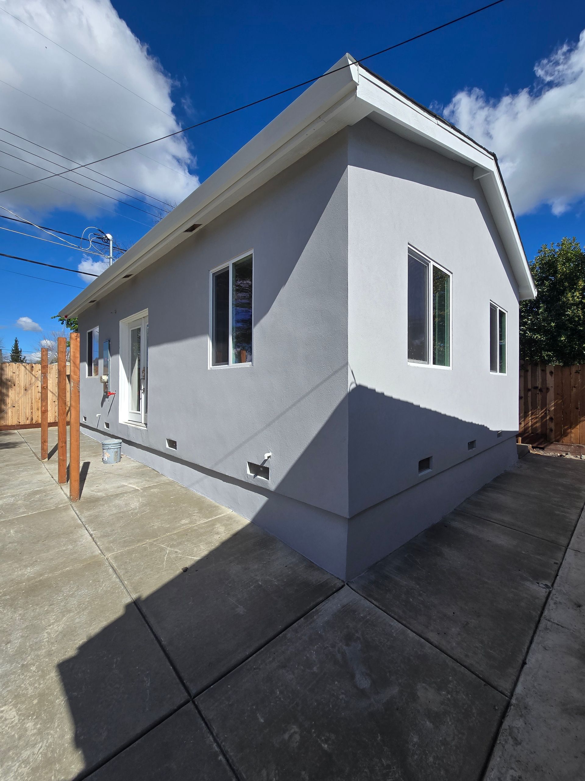 White house exterior with gray trim, concrete walkway, and blue sky.
