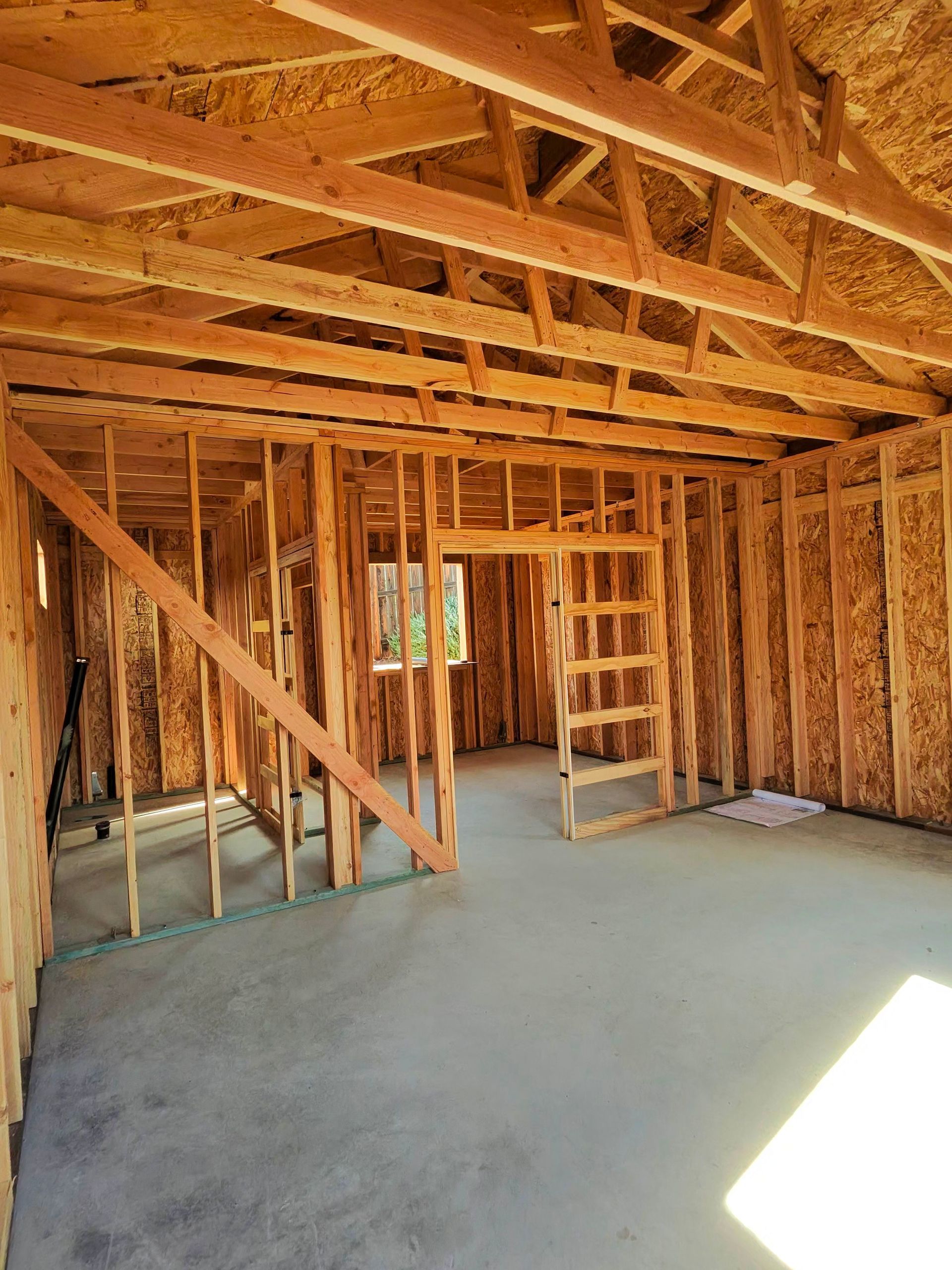 Interior of an unfinished wooden house framing with exposed rafters and concrete floor