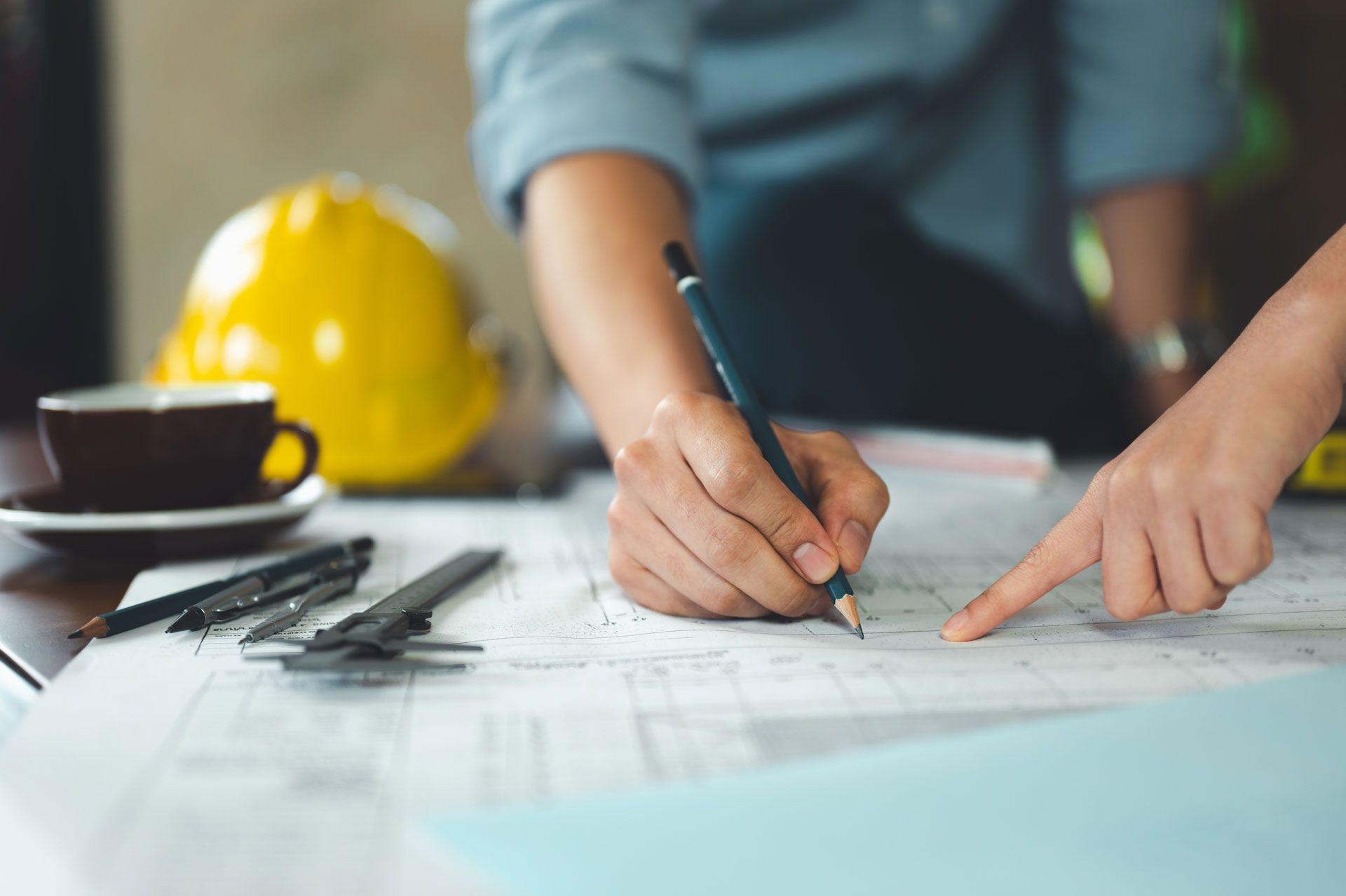 Person marking blueprint beside yellow hard hat on a table