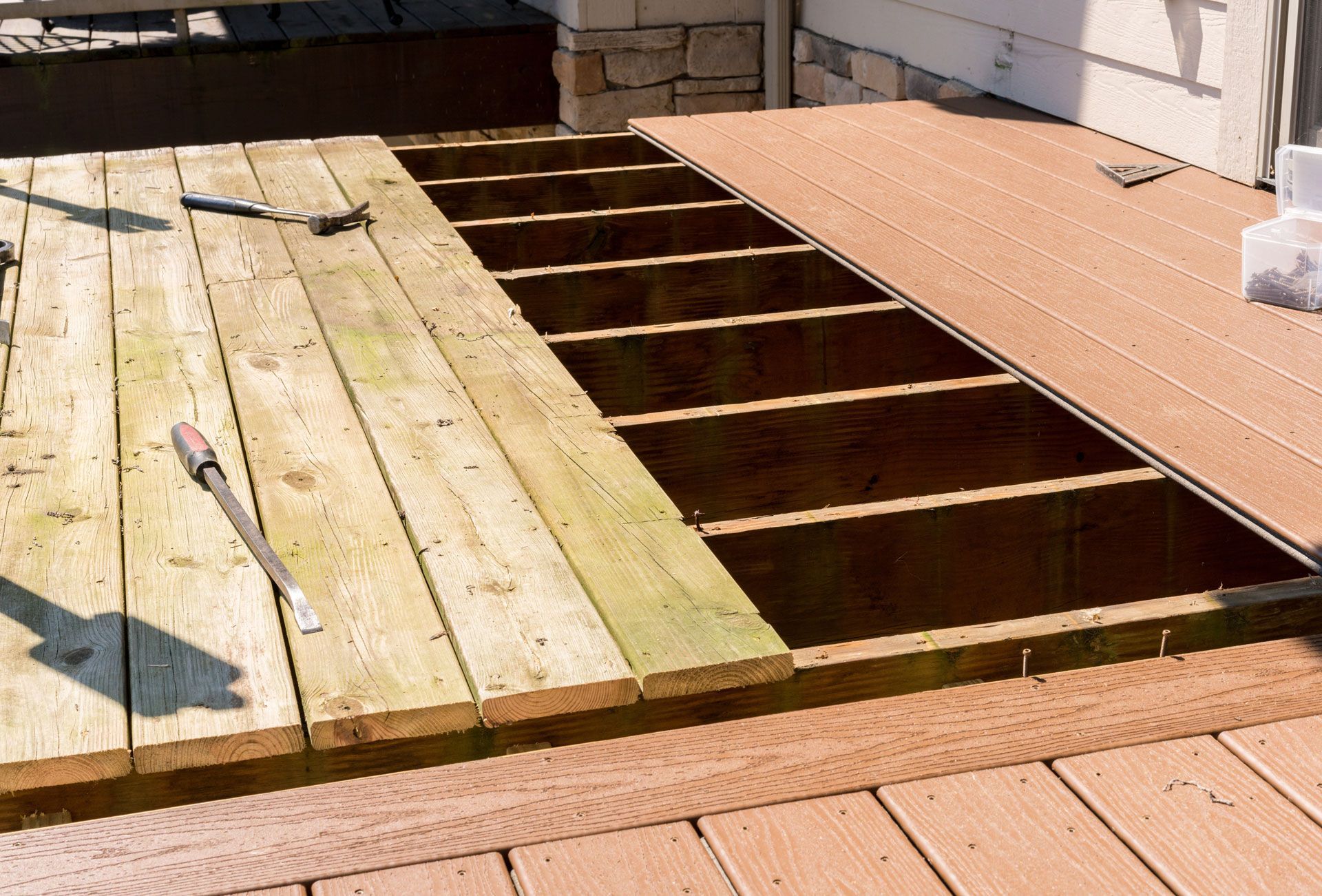 Partially removed wooden deck revealing open joists beside a tan patio