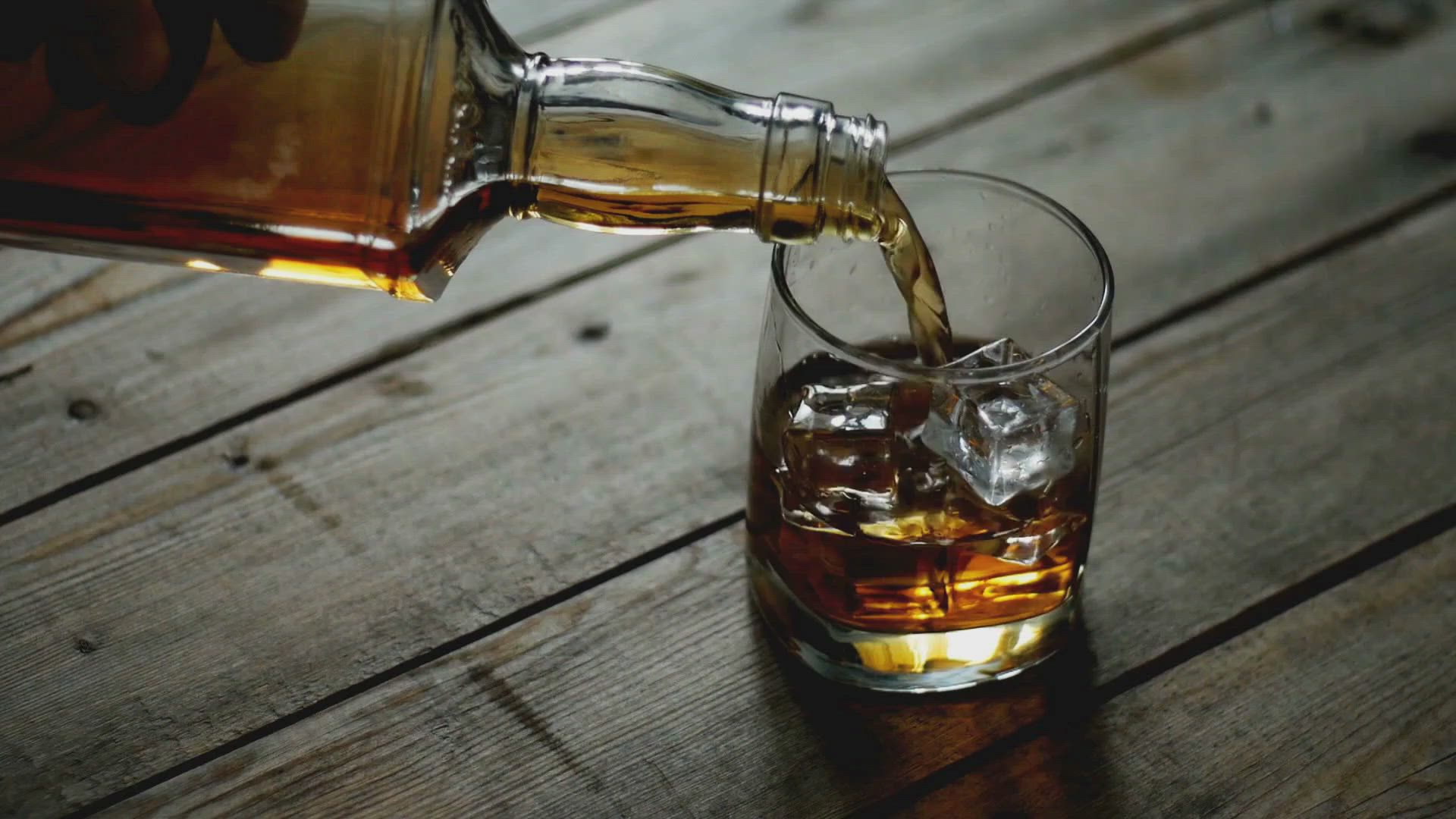 Whiskey being poured from a bottle into a glass with ice cubes, on a wooden surface.