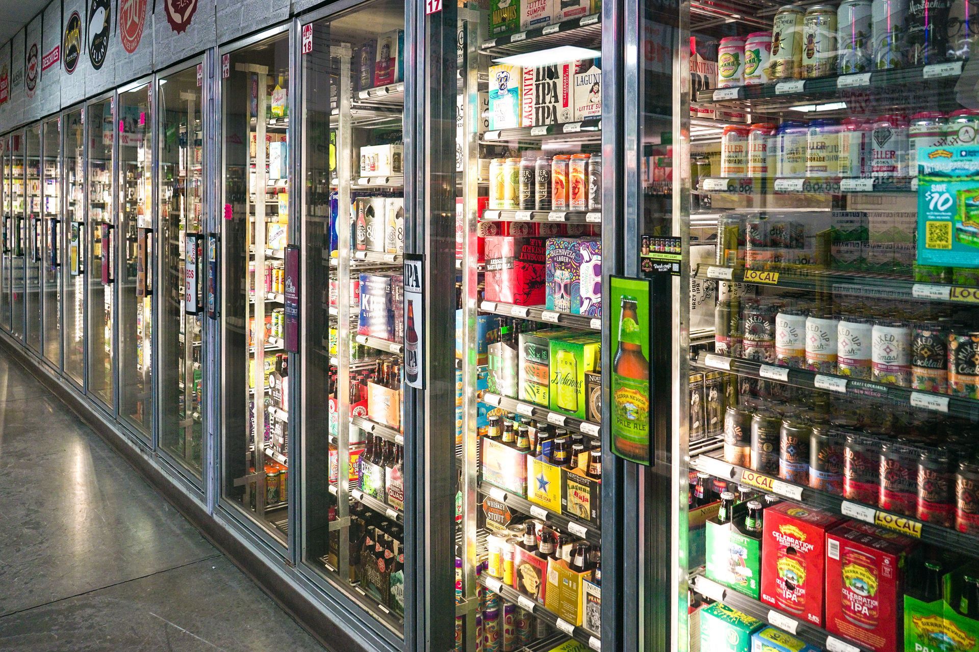 Refrigerated beverage cases in a brightly lit grocery store aisle, filled with various drinks.