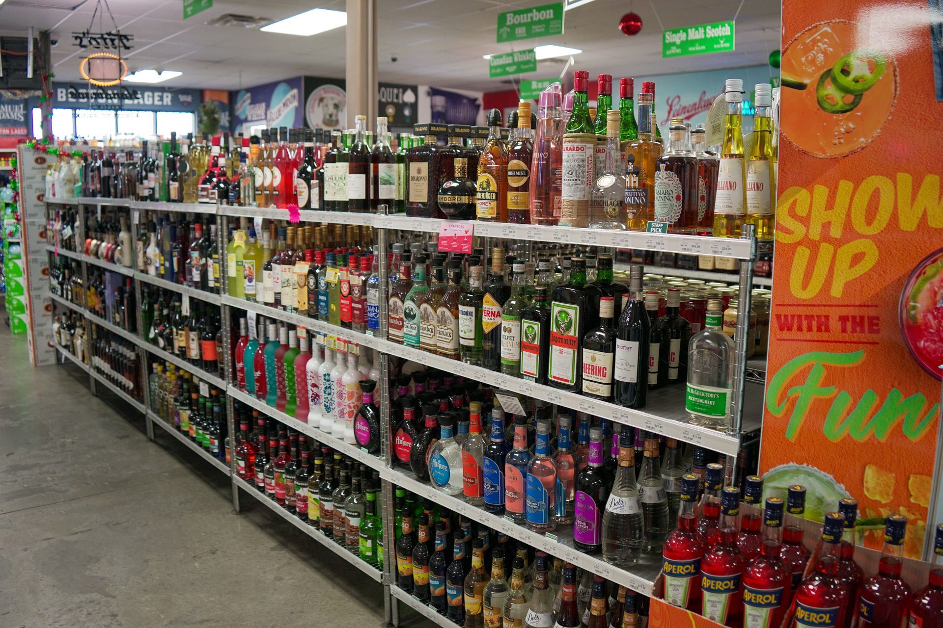 Shelves of liquor bottles in a store. Reds, greens, and whites are prominent, with signage overhead.