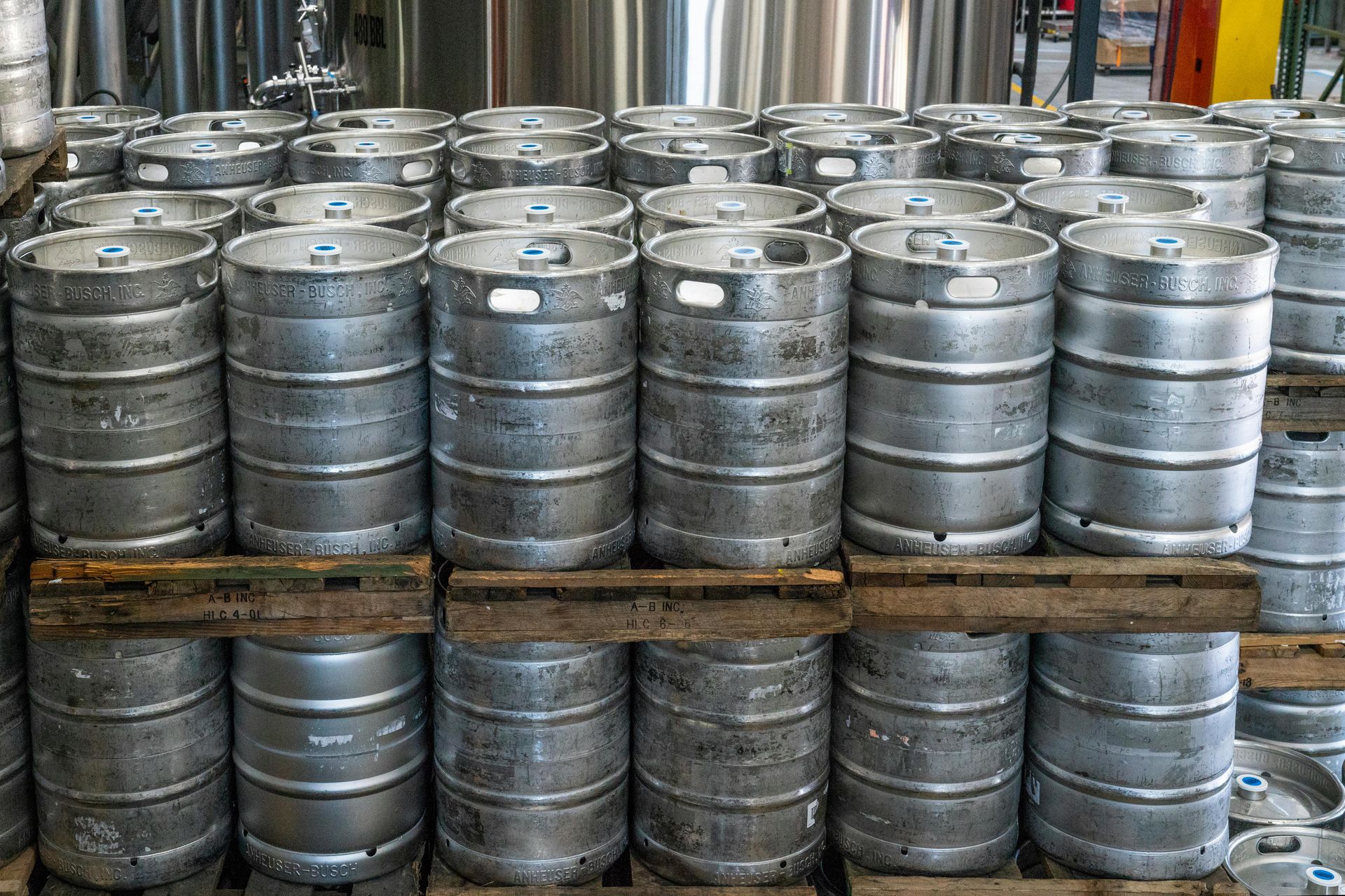 Stacks of silver beer kegs on wooden pallets in a warehouse.