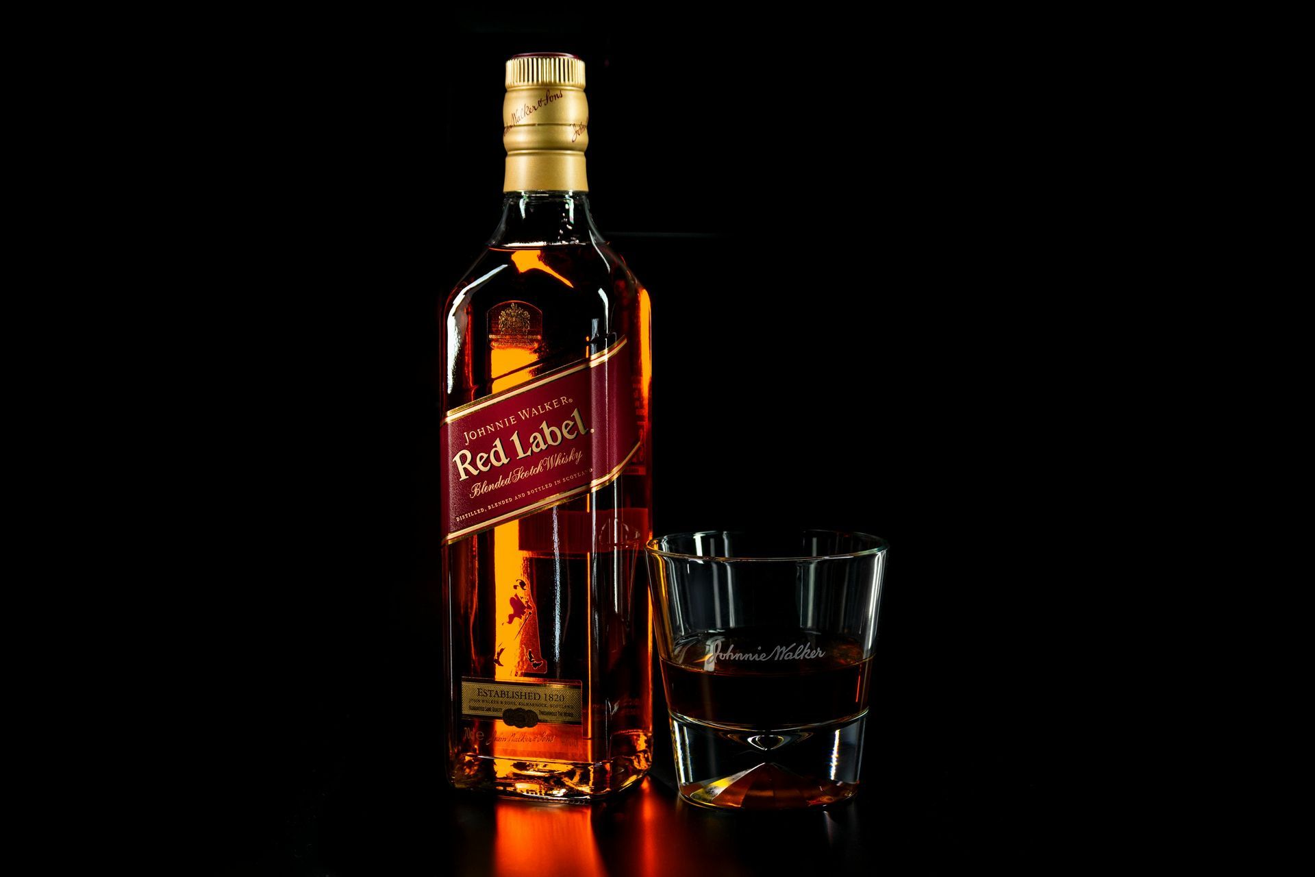 Bottle of Johnnie Walker Red Label whiskey next to a glass of whiskey, both on a black background.
