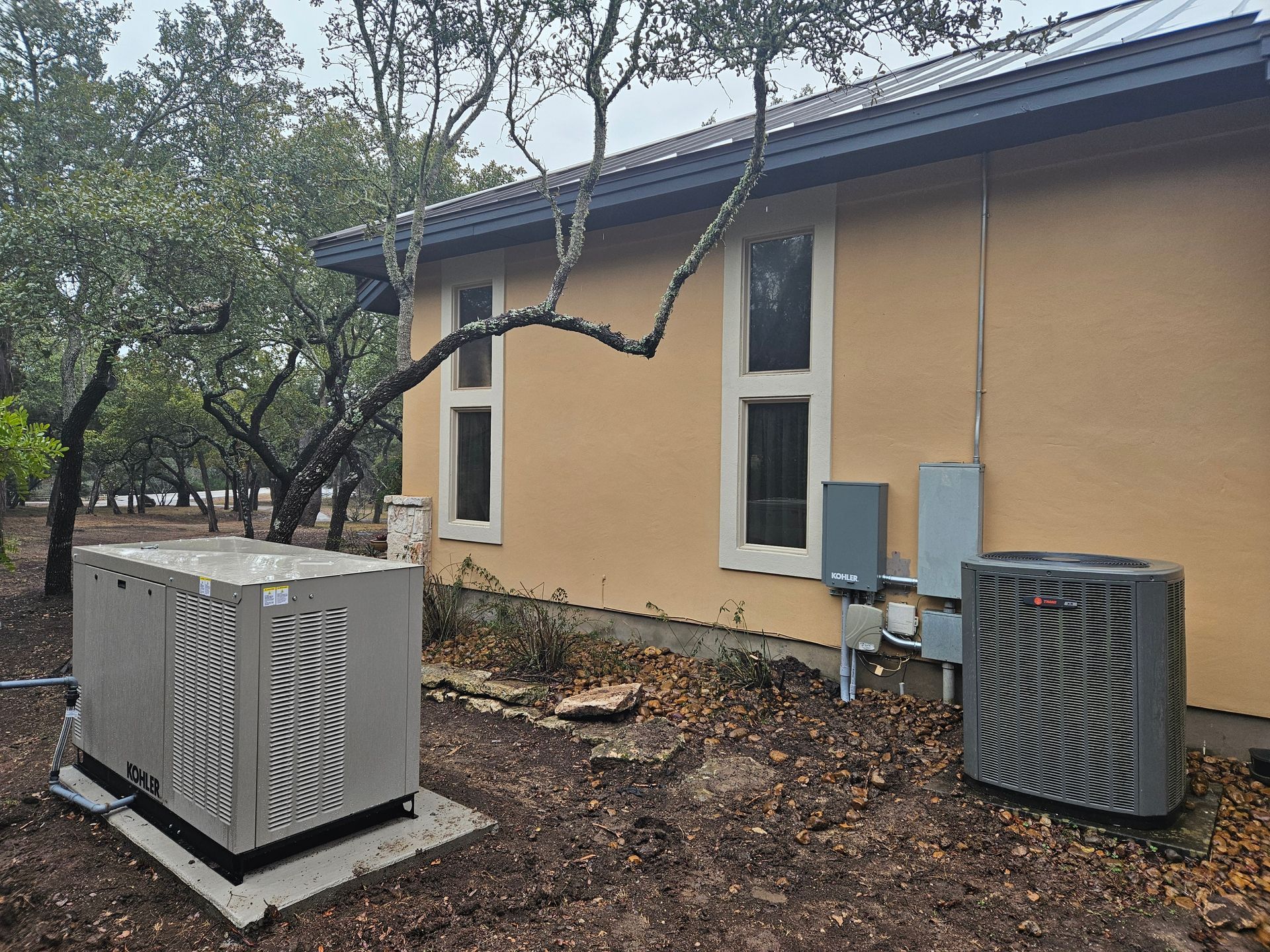 Generator, electrical panel, and AC unit outside a beige house with trees on a cloudy day.