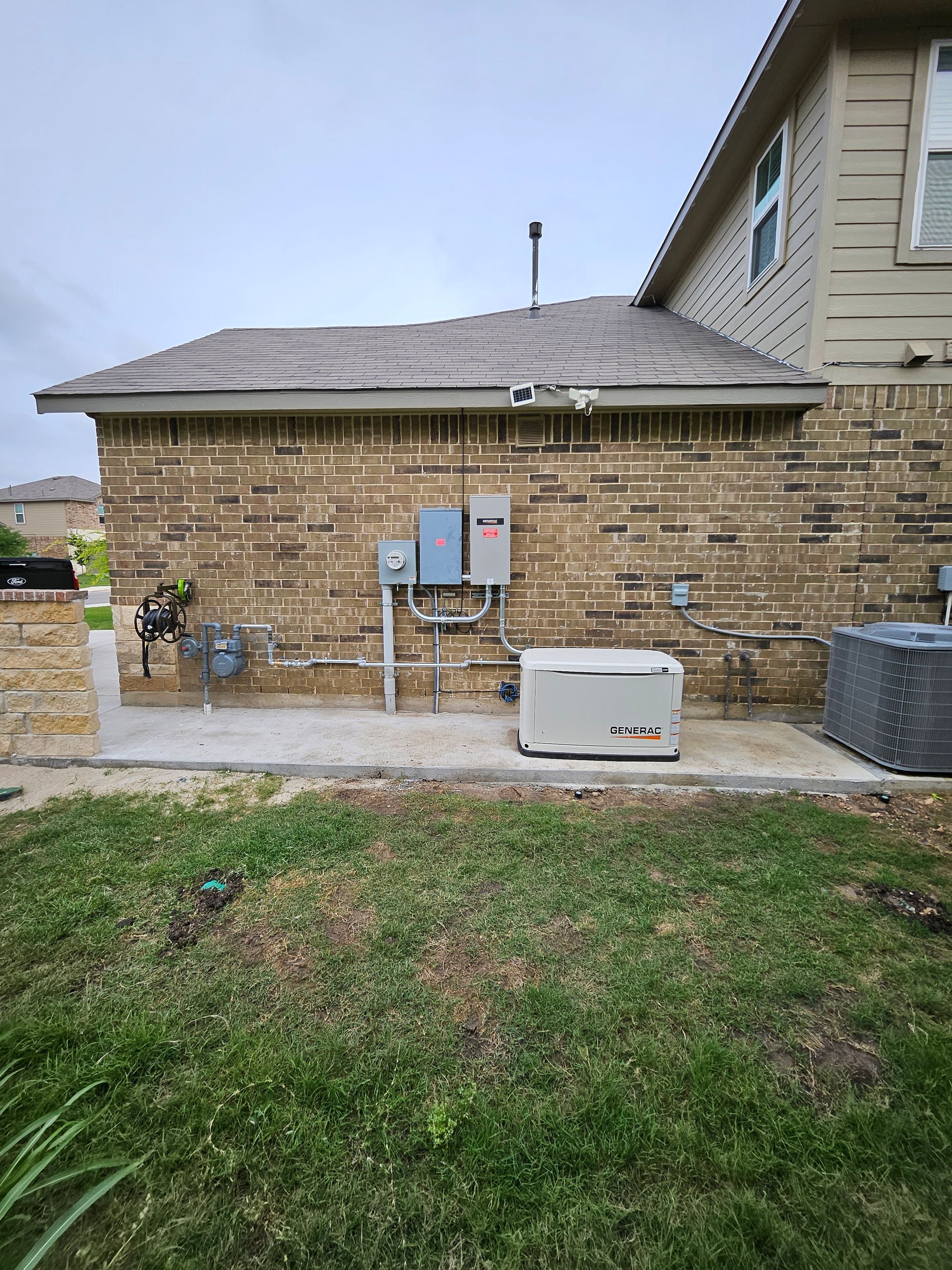 Brick house exterior with generator, electrical panel, and air conditioner on a concrete pad, surrounded by grass.