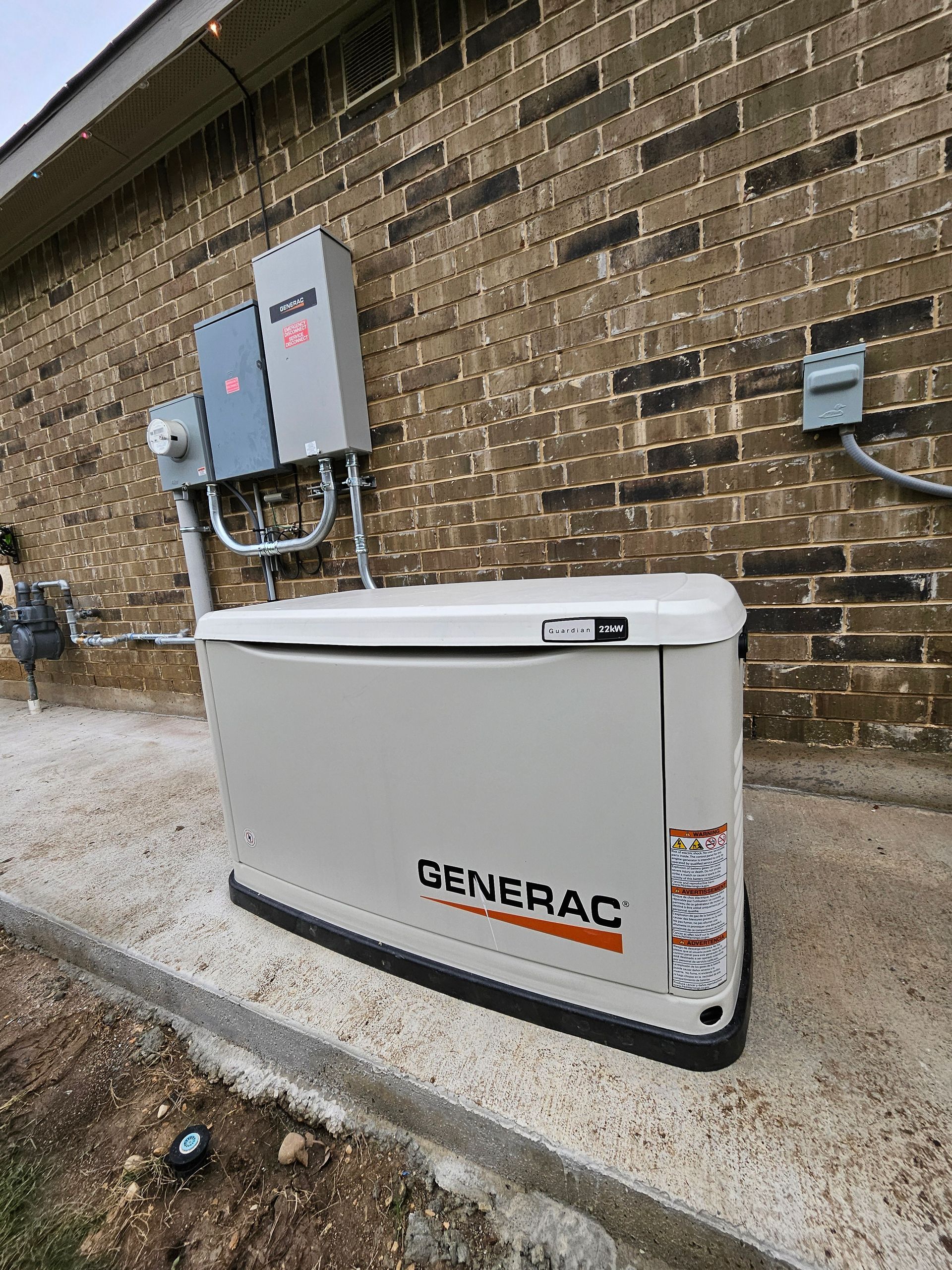 A Generac generator against a brick wall, with electrical boxes mounted above it.