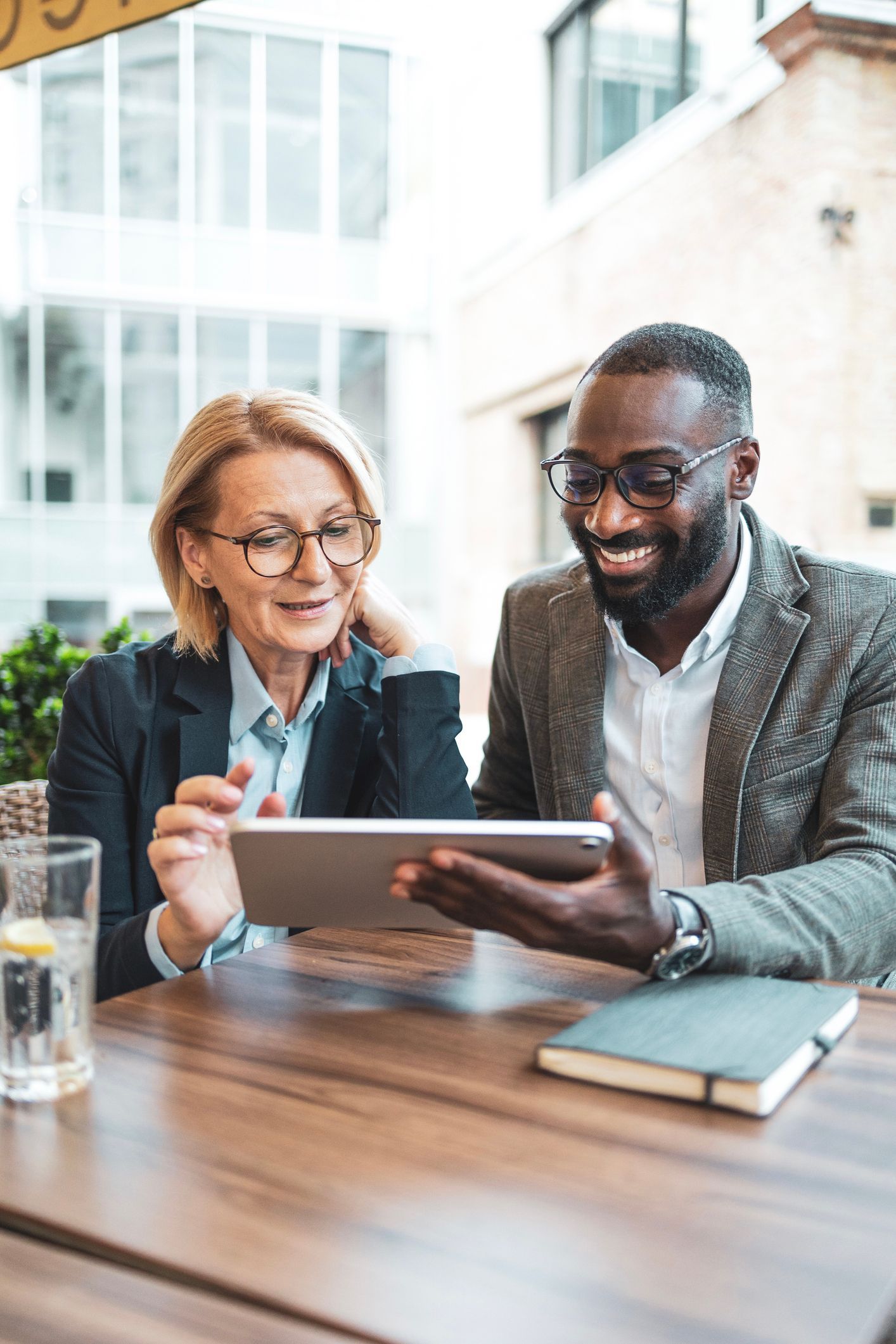 A man and a woman are sitting at a table looking at a tablet.