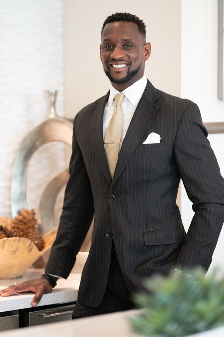 A man in a suit and tie is standing in a kitchen with his hands in his pockets.