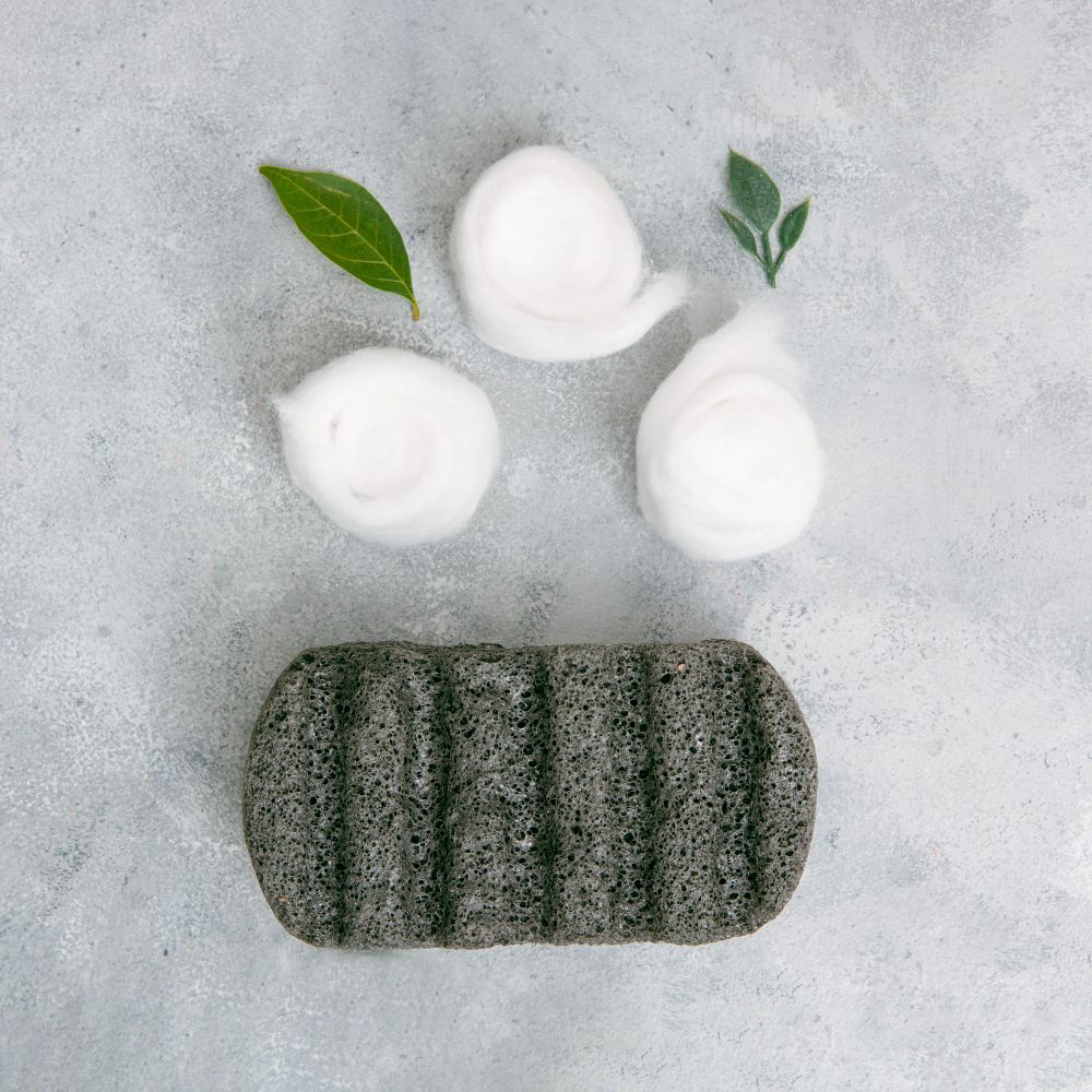 Charcoal soap dish with three foam puffs and two green leaves on a textured grey background.