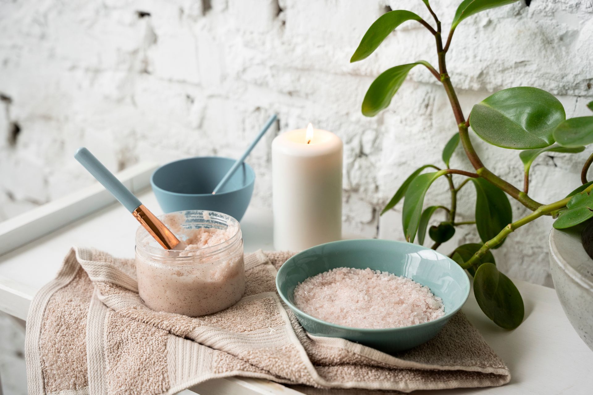 Spa setup: face mask in jar, bowl with bath salts, candle, plant, and blue bowls on a white tray.
