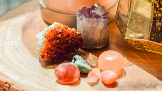 Close-up of crystals and stones on a wooden surface, with a candle and lantern in the background.