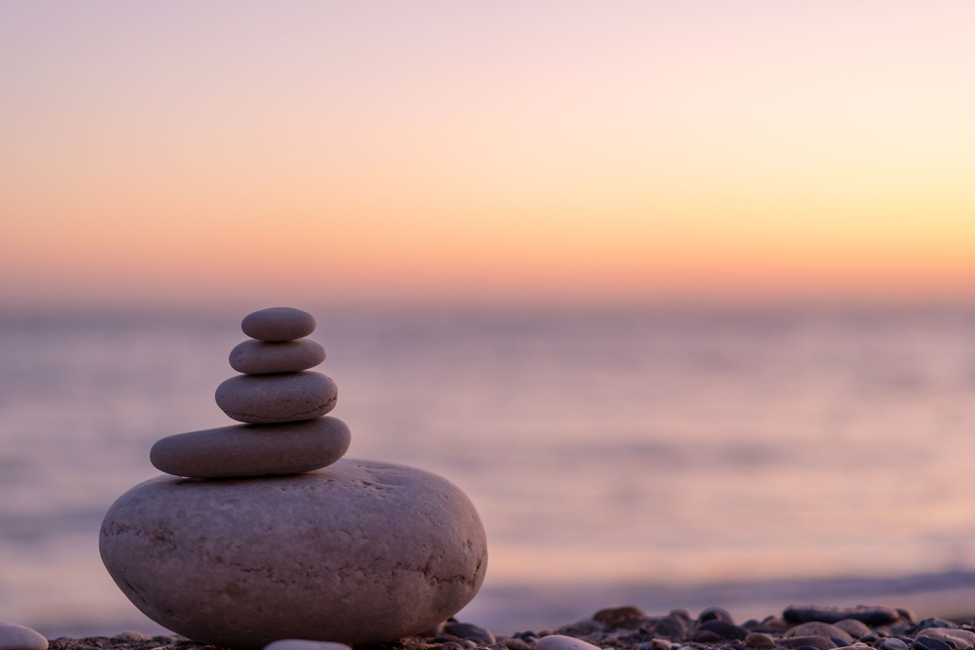 Stack of smooth stones balanced on a beach with a sunset in the background.